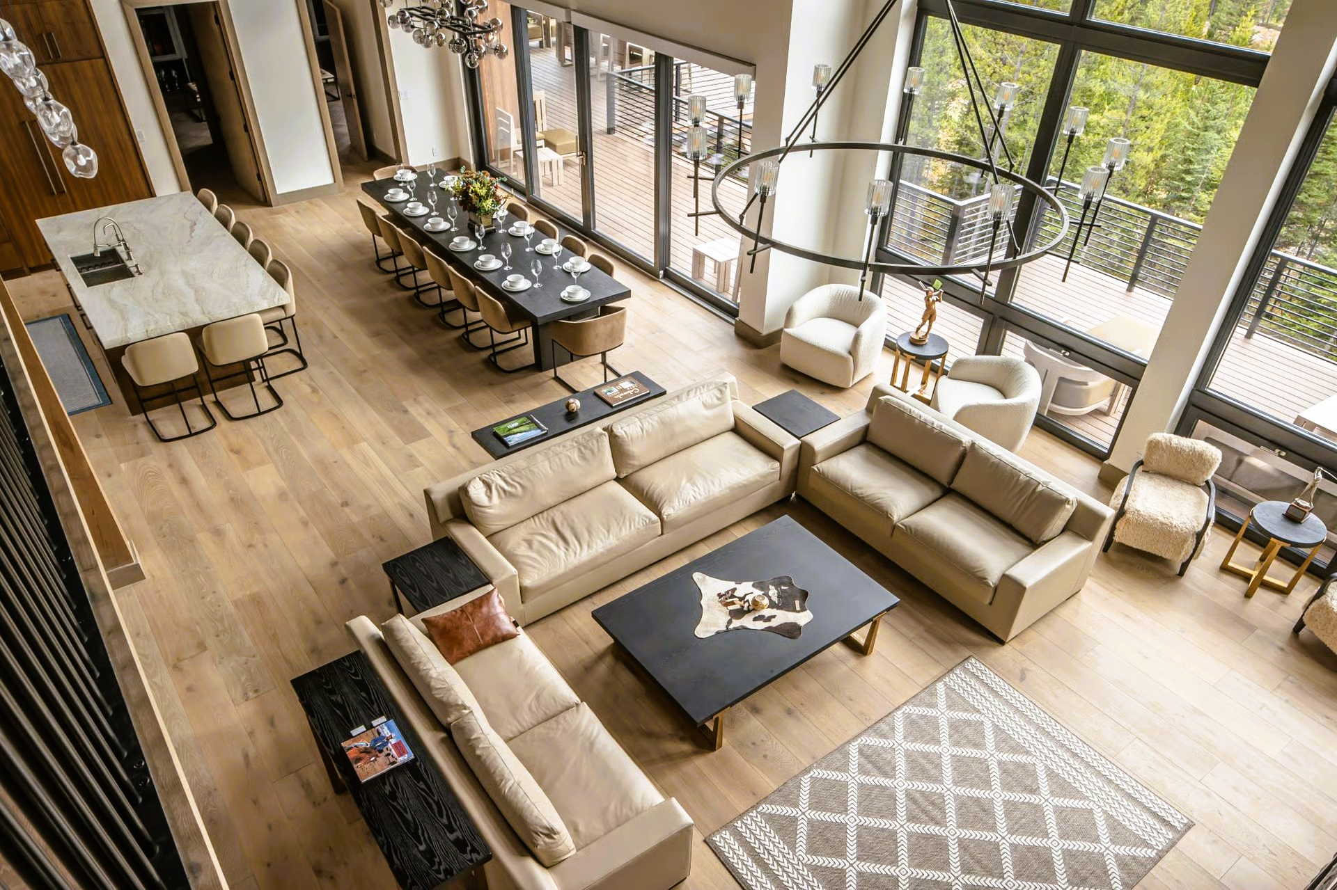 Spacious modern living room with hardwood floors, large windows, multiple beige sofas, and a long dining table.