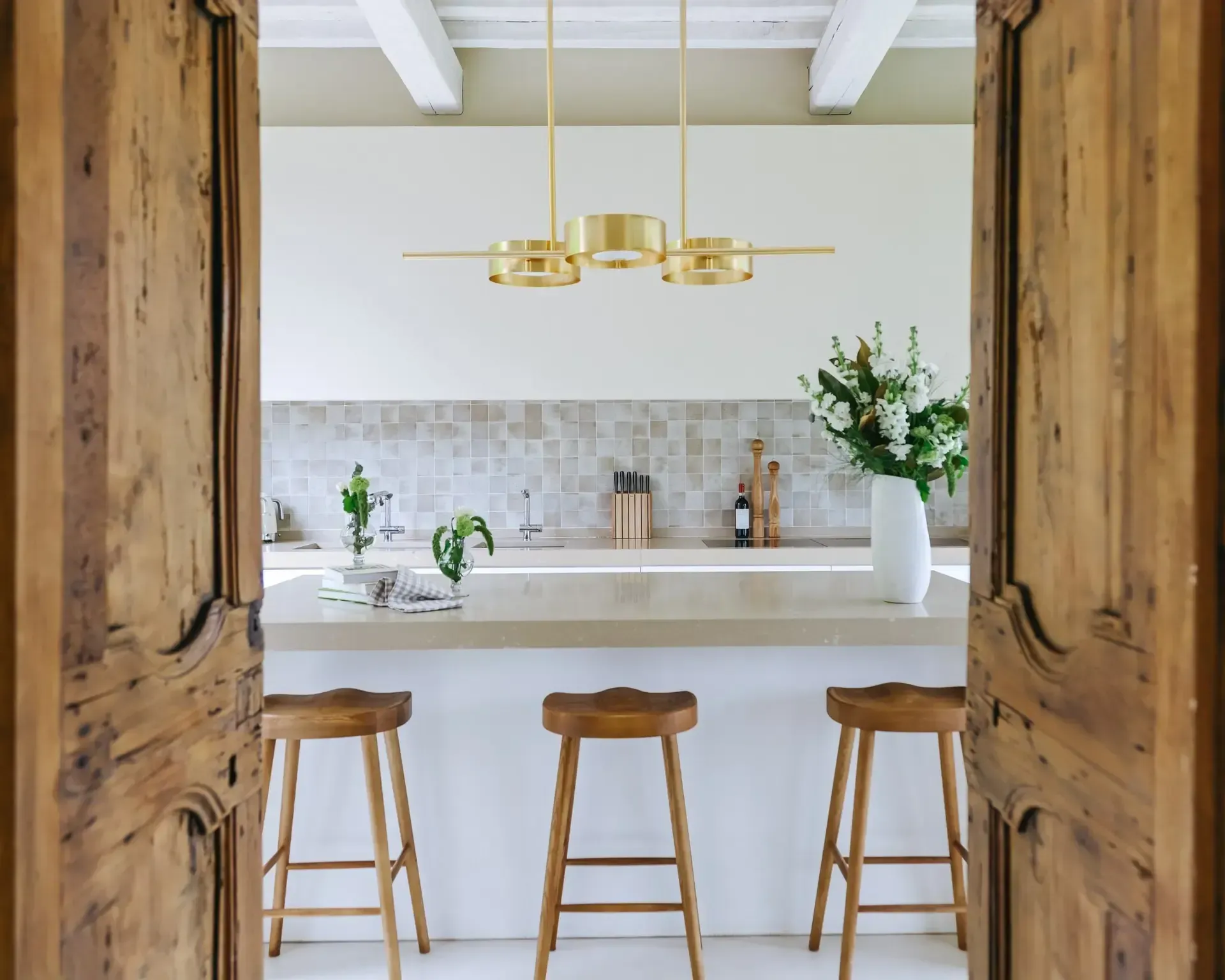 Rustic kitchen interior framed by wooden doors; includes light fixture, stools, and countertop.