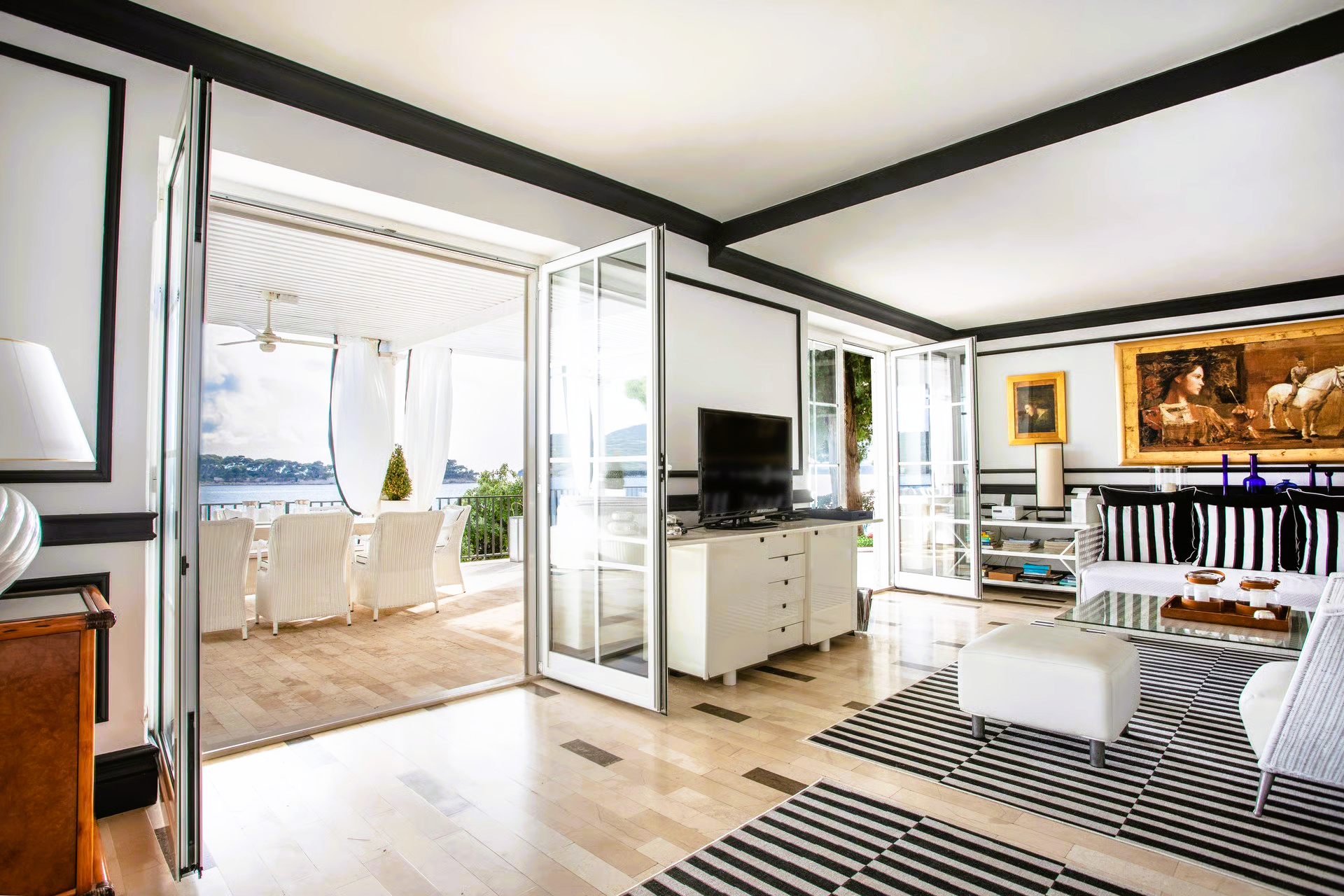 Living room with open doors to a terrace, white walls, black trim, striped rug, and wood flooring.