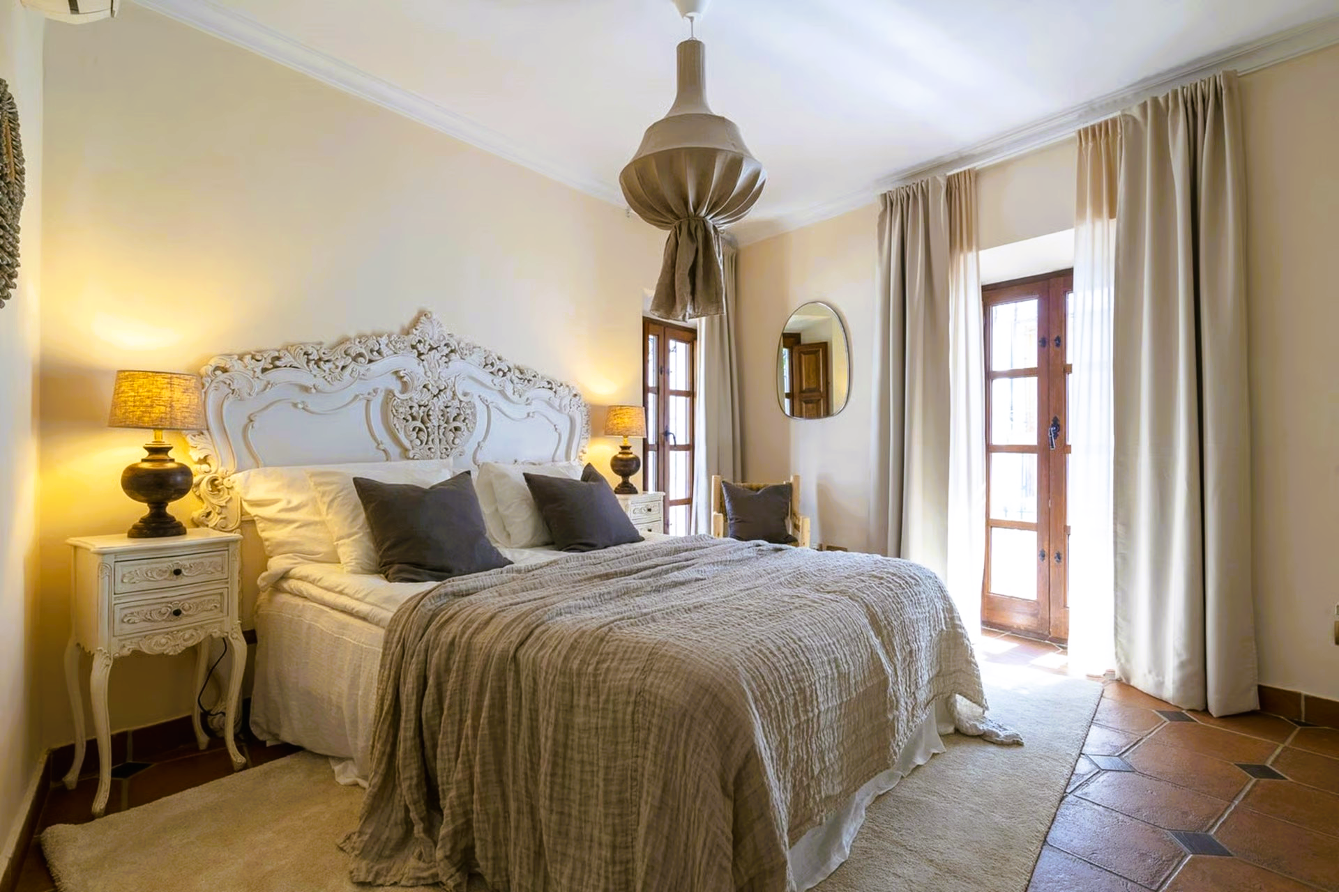Bedroom with a carved white headboard, beige bedspread, nightstand, and doorway to a balcony.