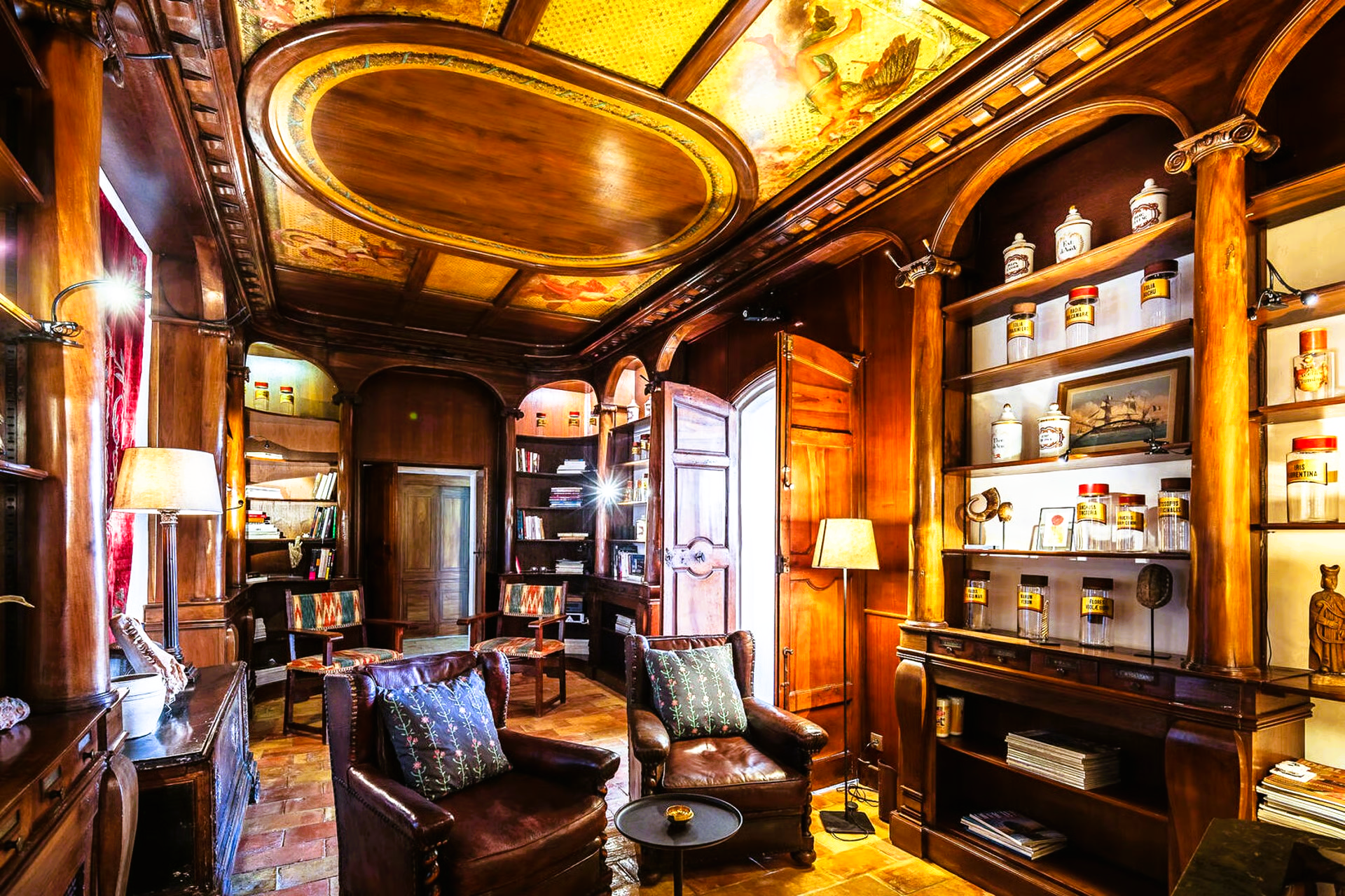 Luxurious library with dark wood paneling, bookshelves, leather chairs, and ornate ceiling art.
