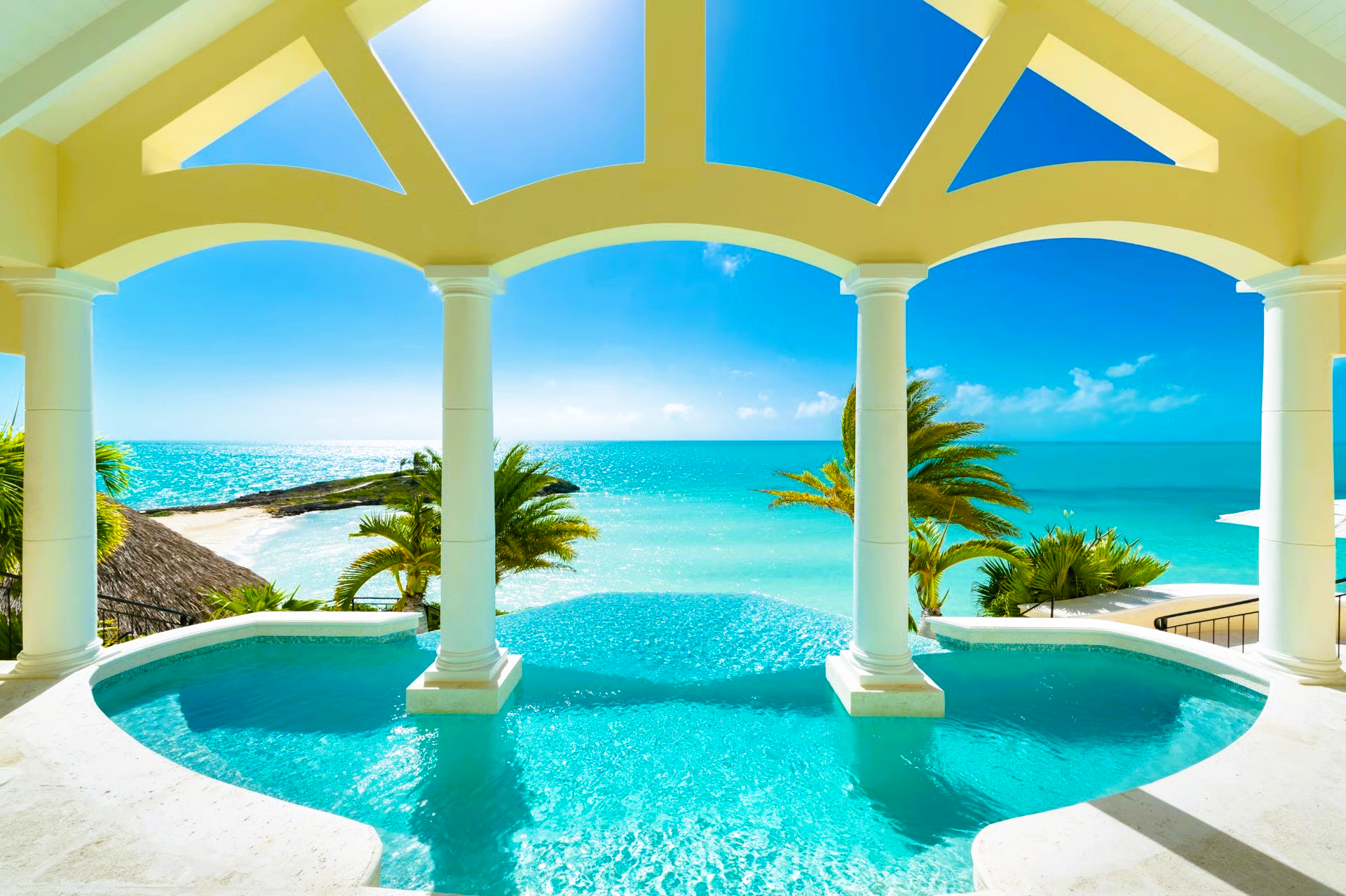 Pool overlooking a turquoise ocean view, framed by white pillars and archways.