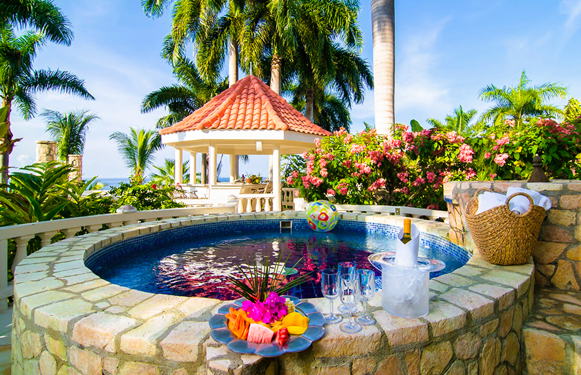 Hot tub with champagne, flowers, and a gazebo in a tropical setting.