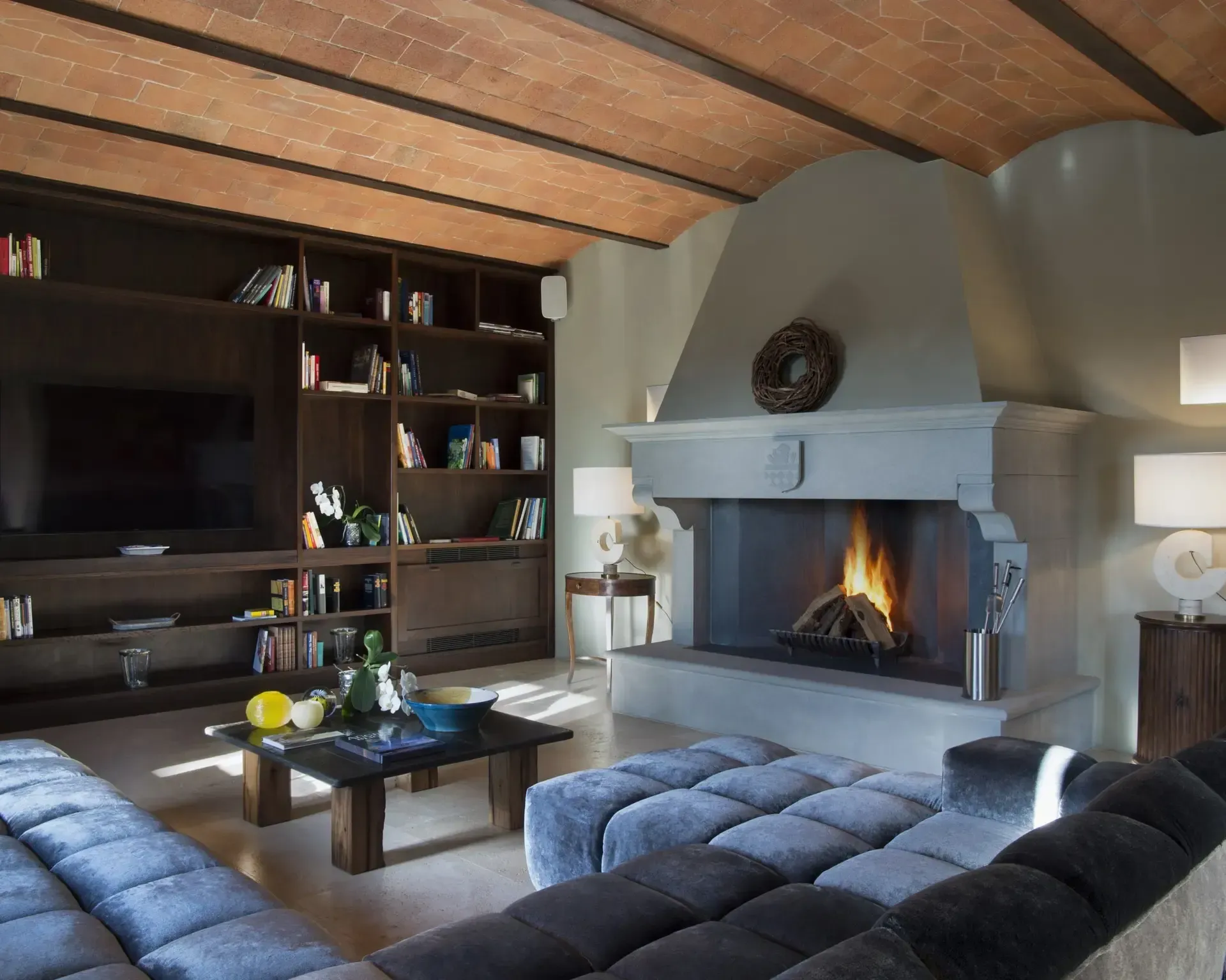 Cozy living room with fireplace, bookshelves, dark sofa, and warm lighting.