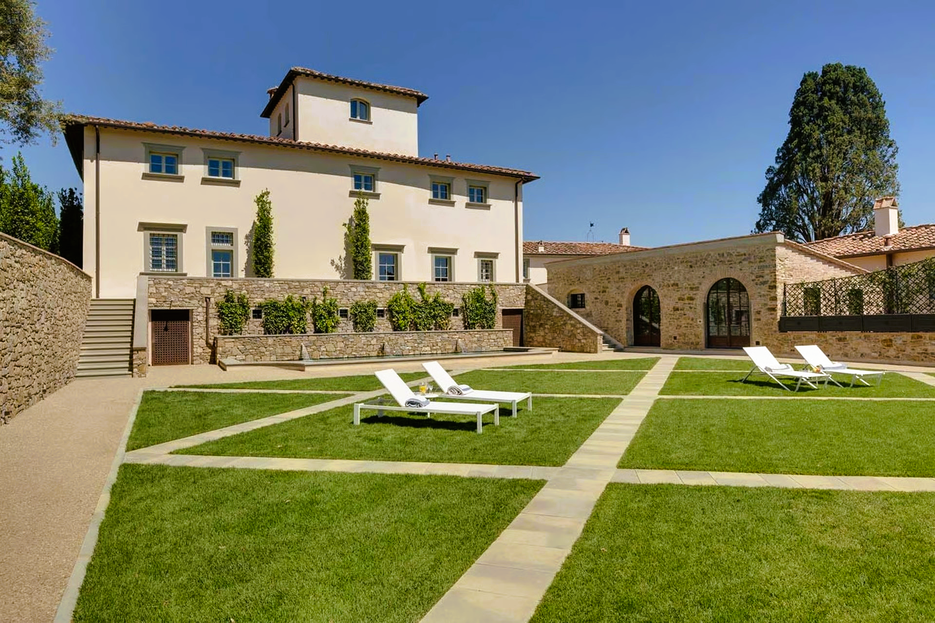 Exterior view of a villa with a square lawn, lounge chairs, and stone walkways.