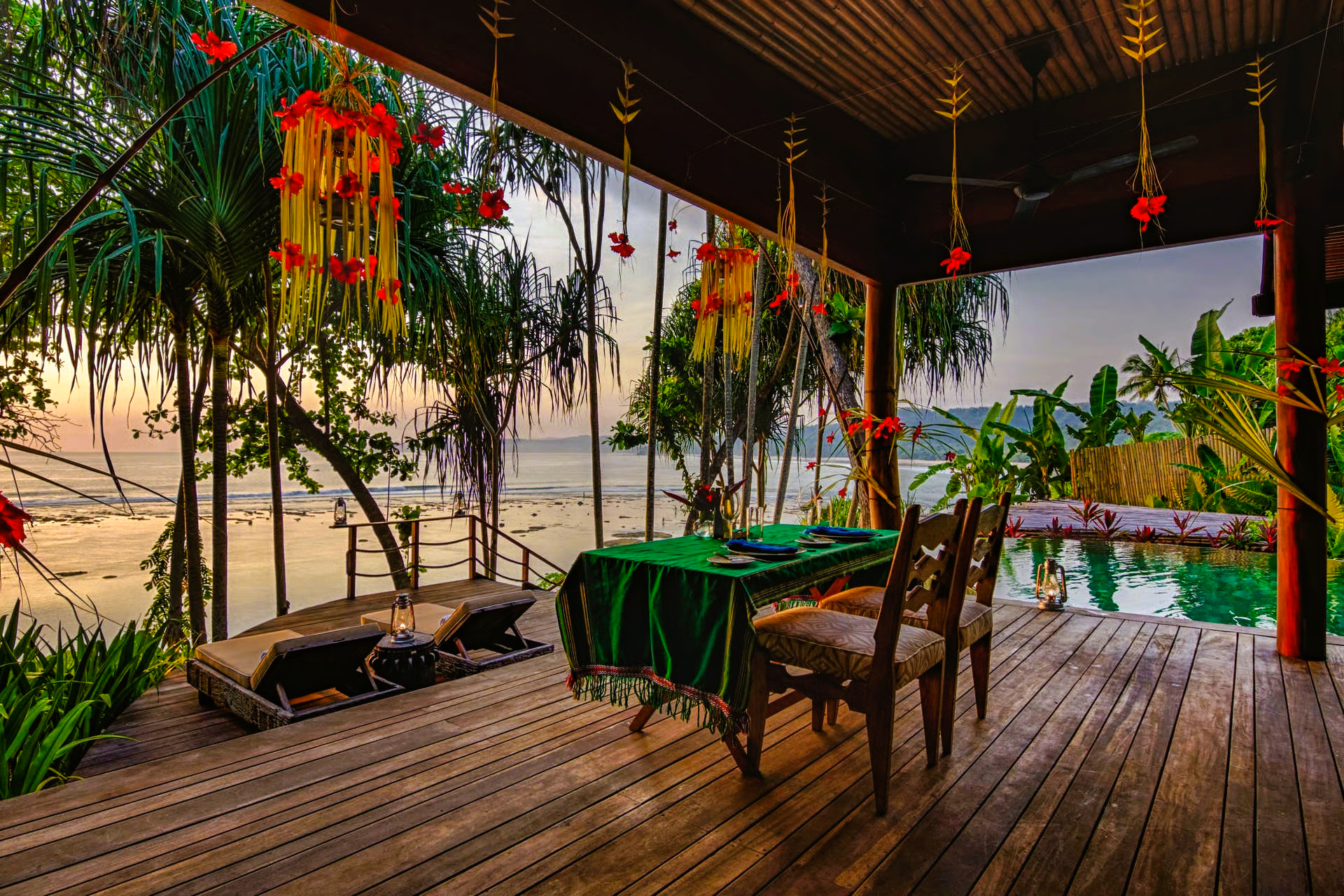 Wooden patio overlooking water with table set for dining and hanging decorations.