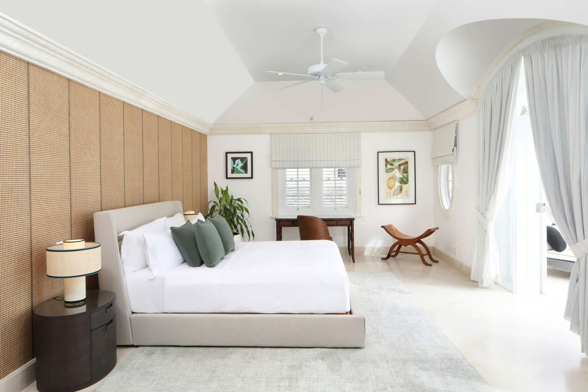 Bright bedroom with a bed, nightstand, desk, and white curtains. Wooden wall paneling and art.
