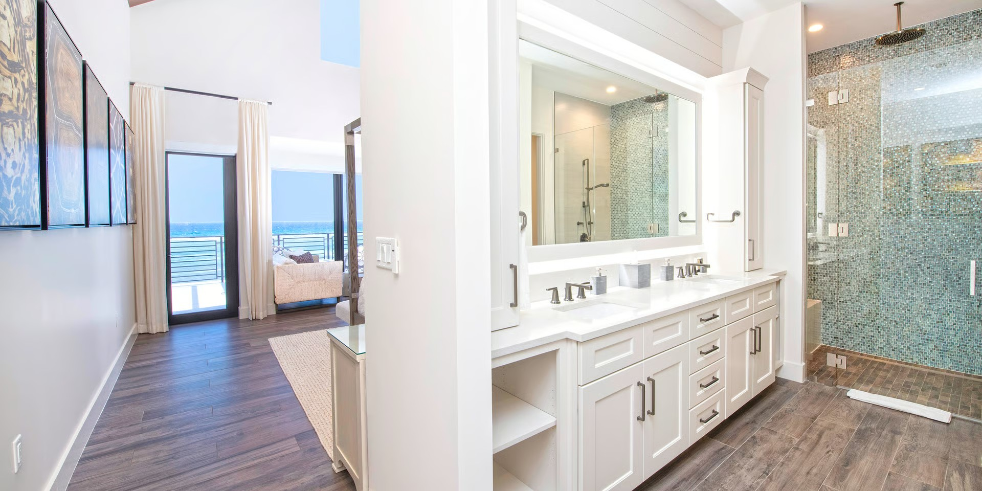 Bathroom with a long white vanity, walk-in shower, and a hallway leading to a view of the ocean.