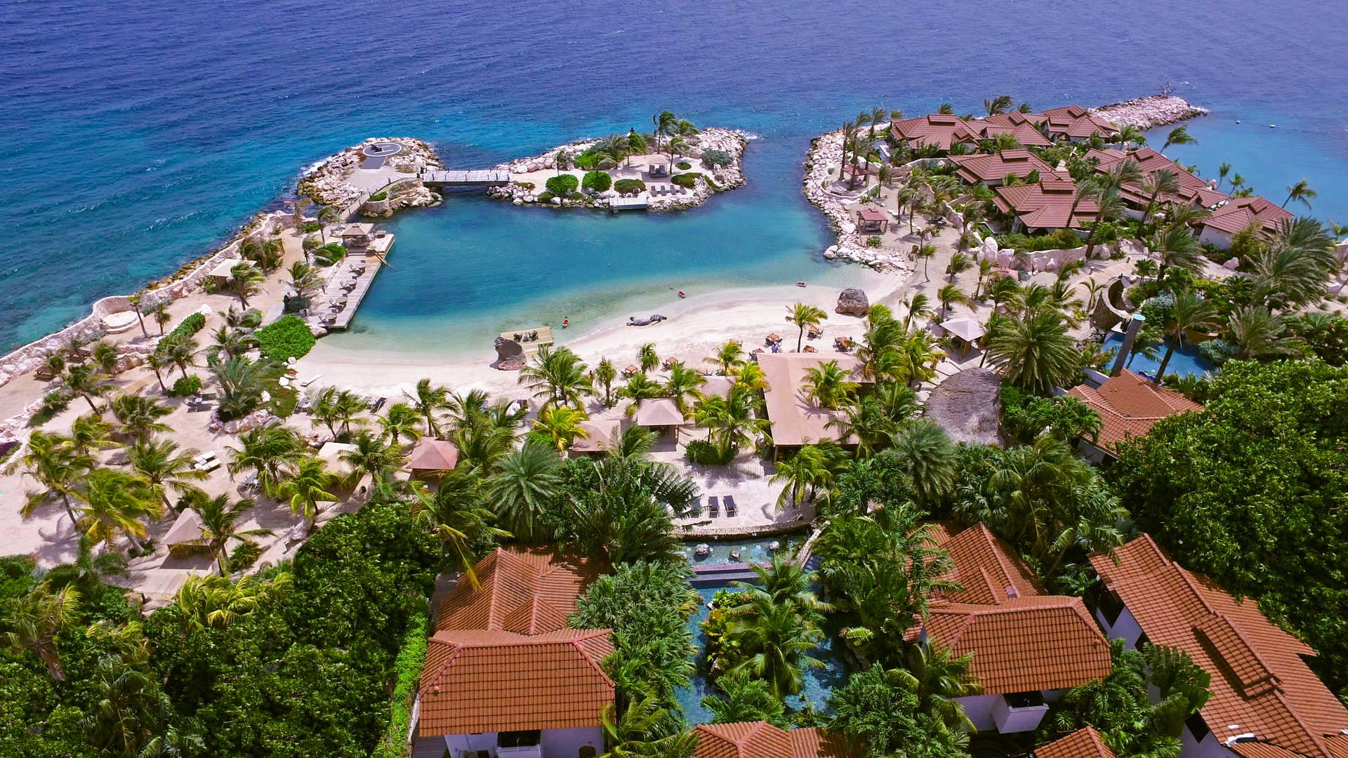 Tropical resort by the ocean with turquoise water, sandy beach, and terracotta rooftops.