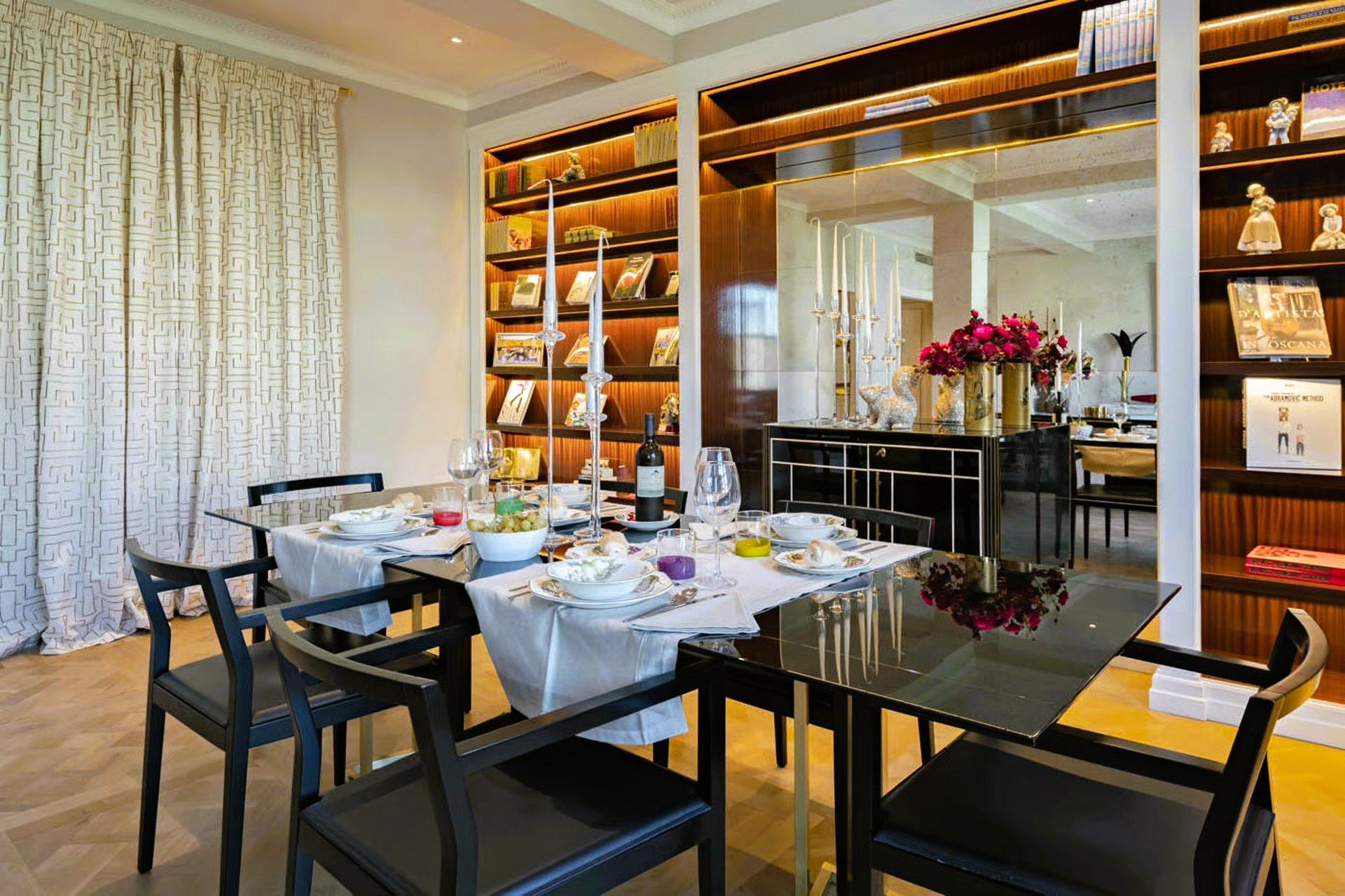 Elegant dining room with a set table, black chairs, and a bookshelf.
