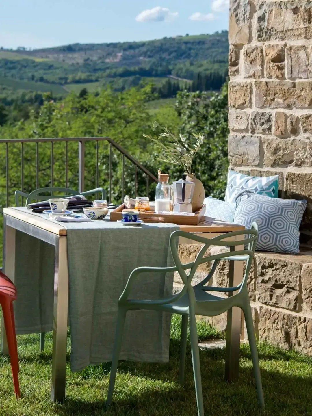 Outdoor table set for a meal with green chairs, blue tablecloth, and a view of rolling hills.