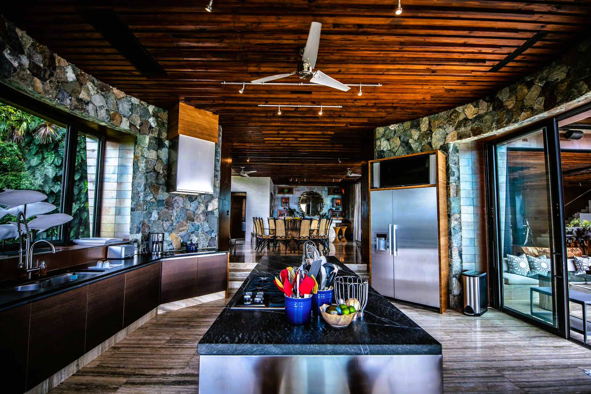 Kitchen with stone walls, stainless steel appliances, island with food/utensils, and a wooden ceiling.