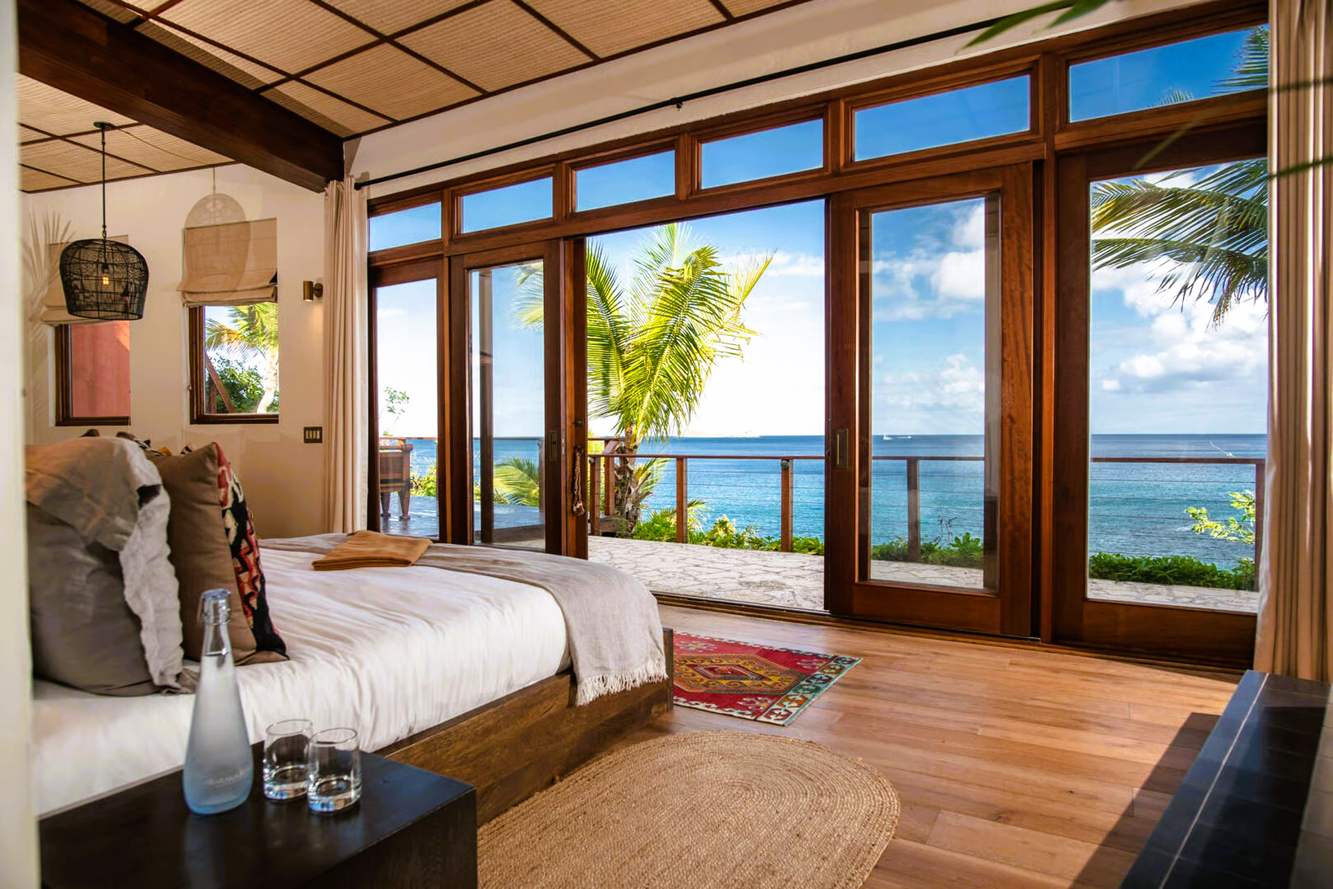 Bedroom with large windows overlooking the ocean; wood trim, neutral tones, sunlight.