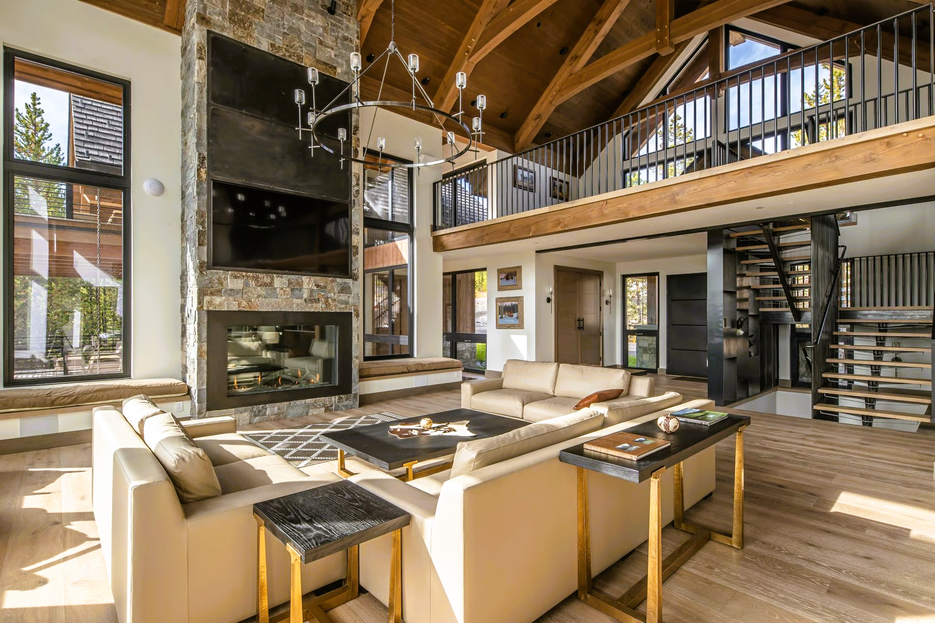 Spacious living room with stone fireplace, light sofas, wooden beams, and a loft.