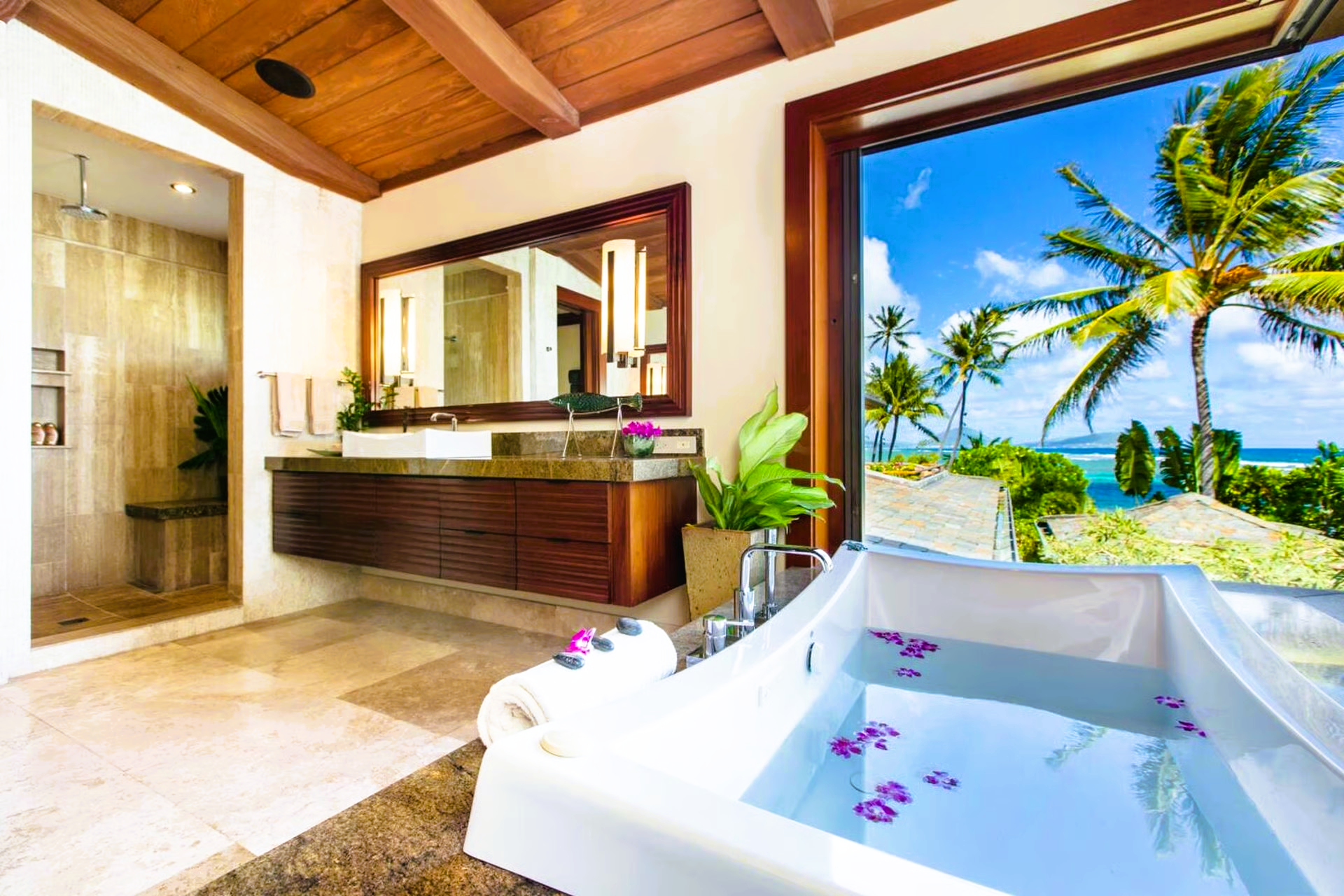 Luxury bathroom with a view of the ocean and palm trees. Features a bathtub, shower, and wooden accents.