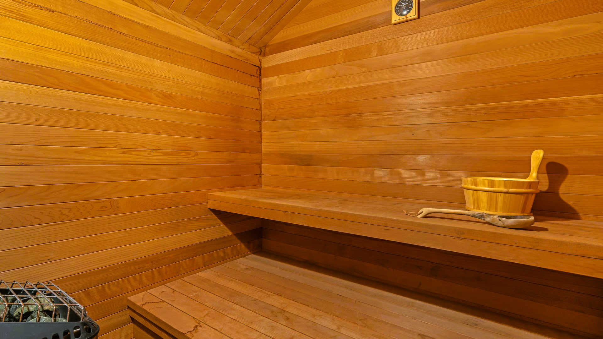 Wooden sauna with benches, a bucket, and heater.