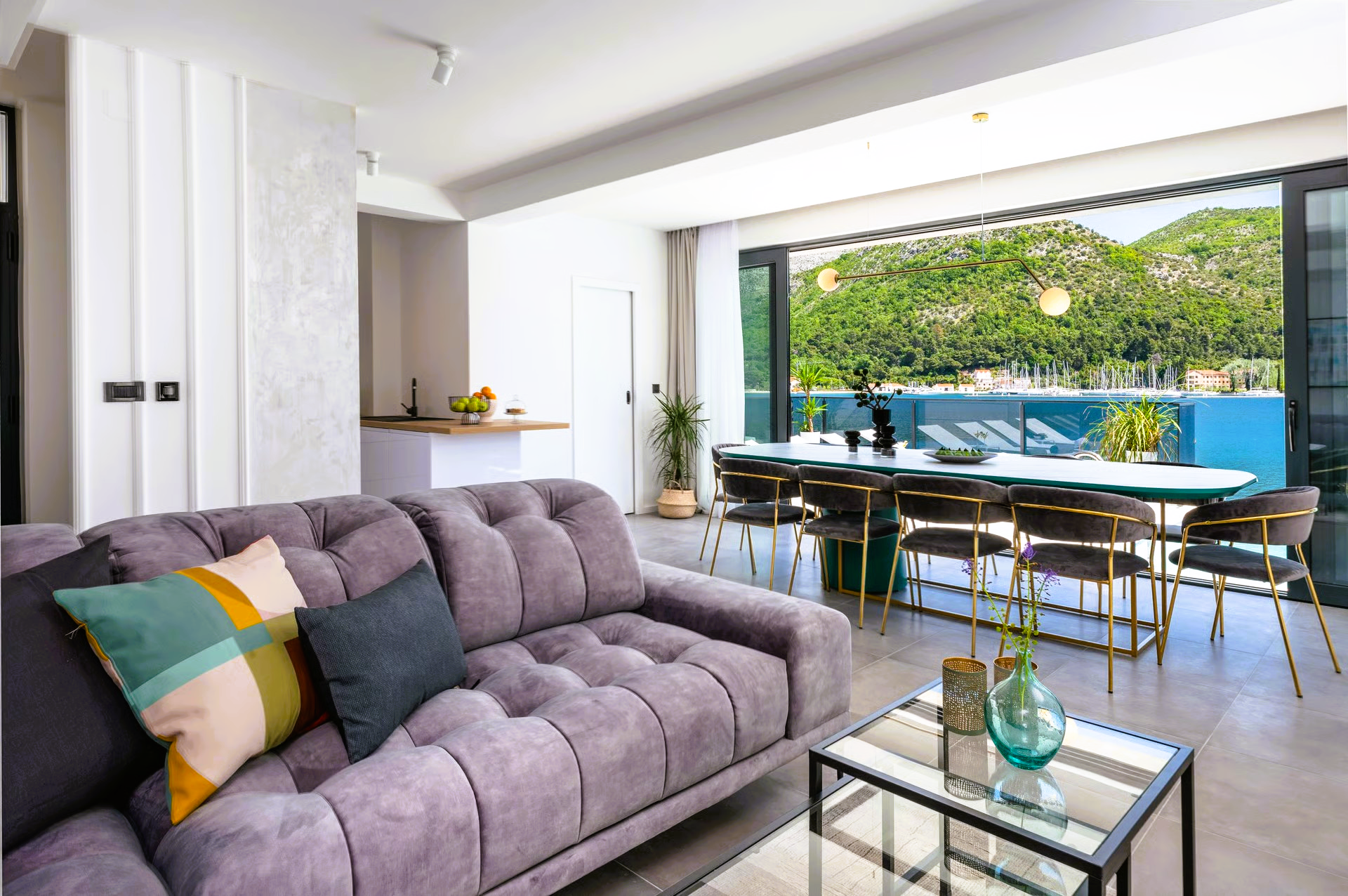 A modern living room with a purple couch, dining table, and sliding doors to a patio with greenery.