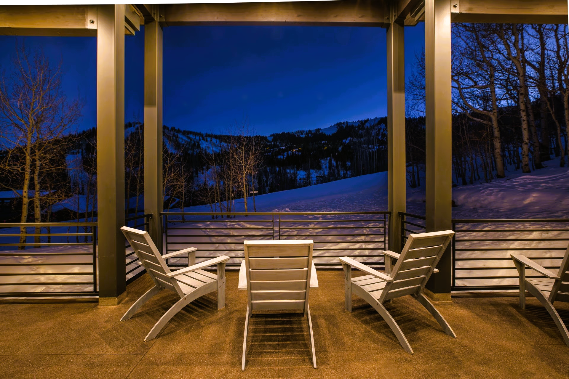 Patio with white chairs overlooking snow-covered mountain landscape at dusk.