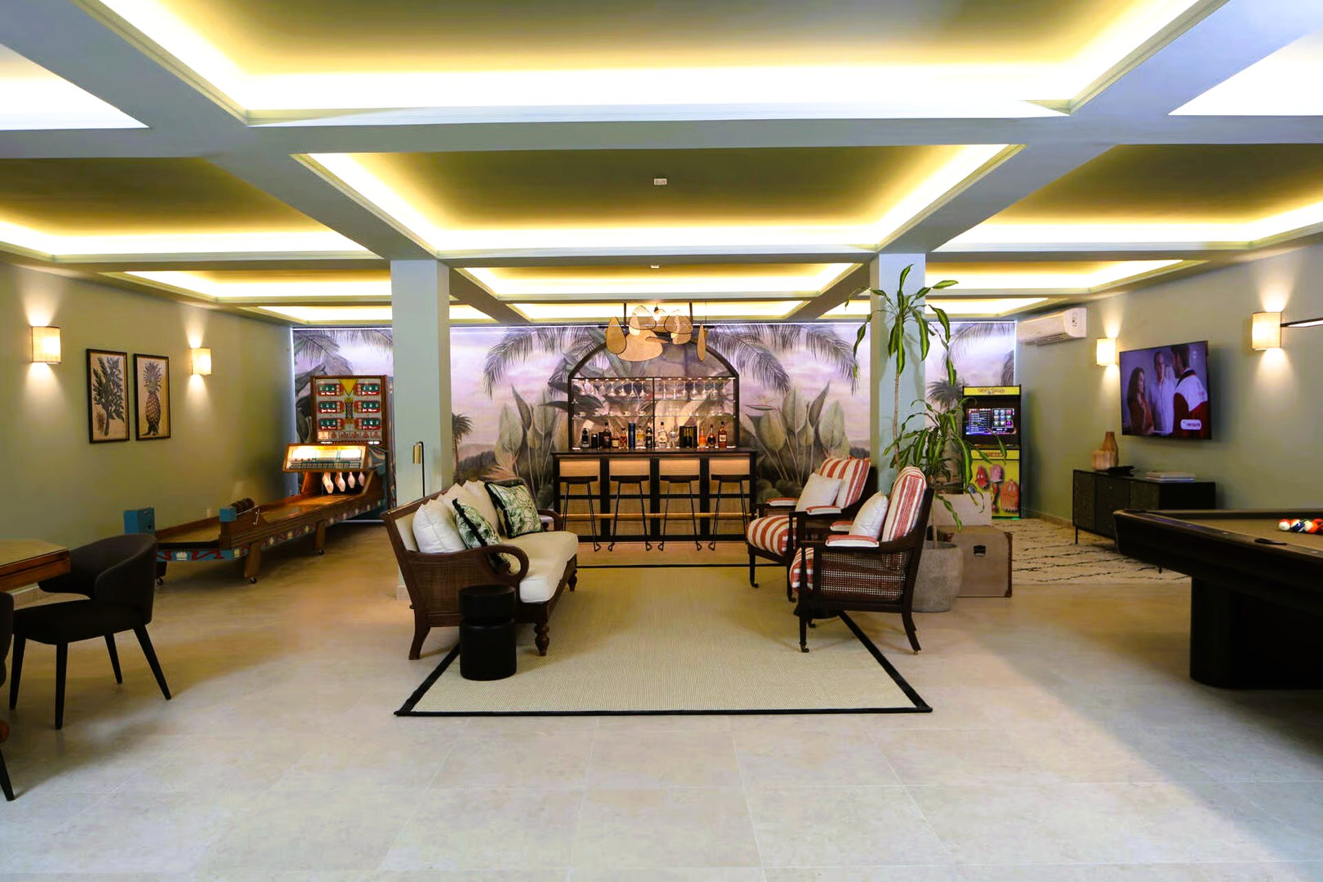Interior lounge with bar, pool table, seating, and arcade game; green and cream tones.