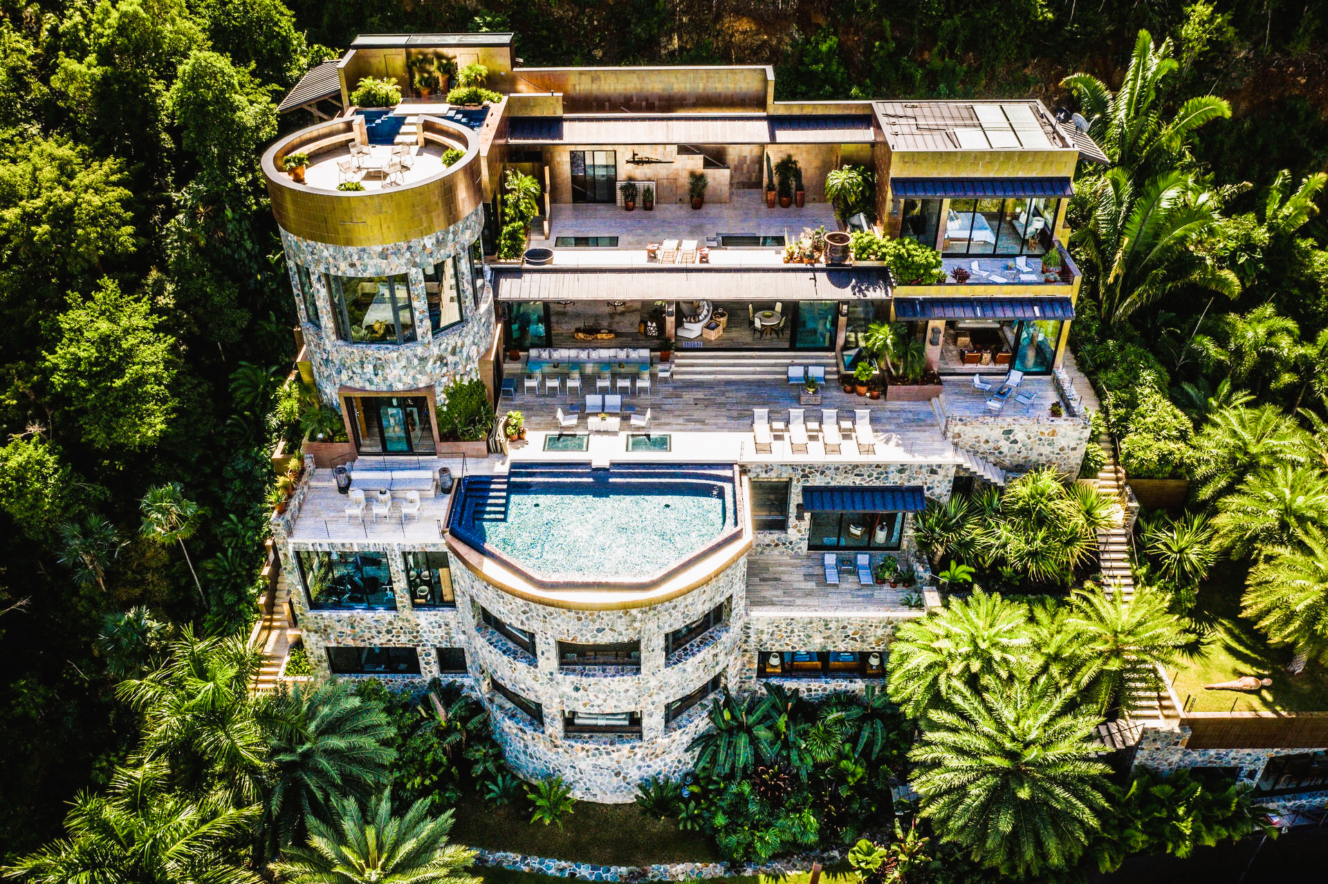Luxurious multi-story mansion with pool, surrounded by lush green trees.
