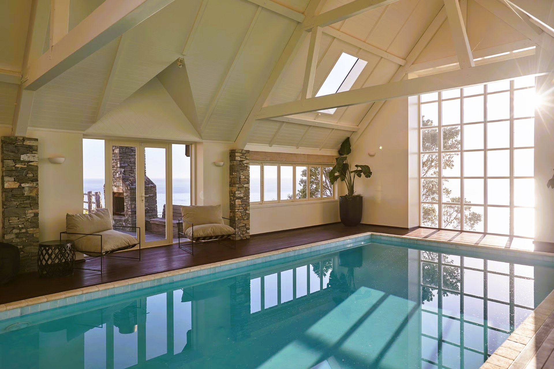 Indoor pool with sunlight, vaulted ceiling, large windows, and a stone fireplace.