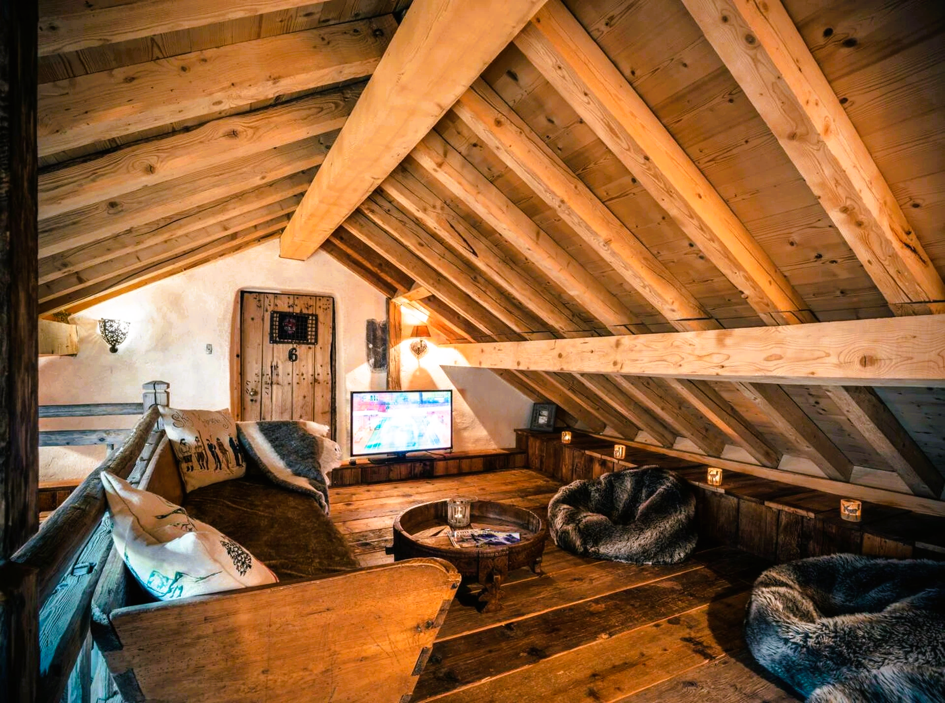 Cozy attic living space with wooden beams, a sofa, beanbag chairs, and a TV.