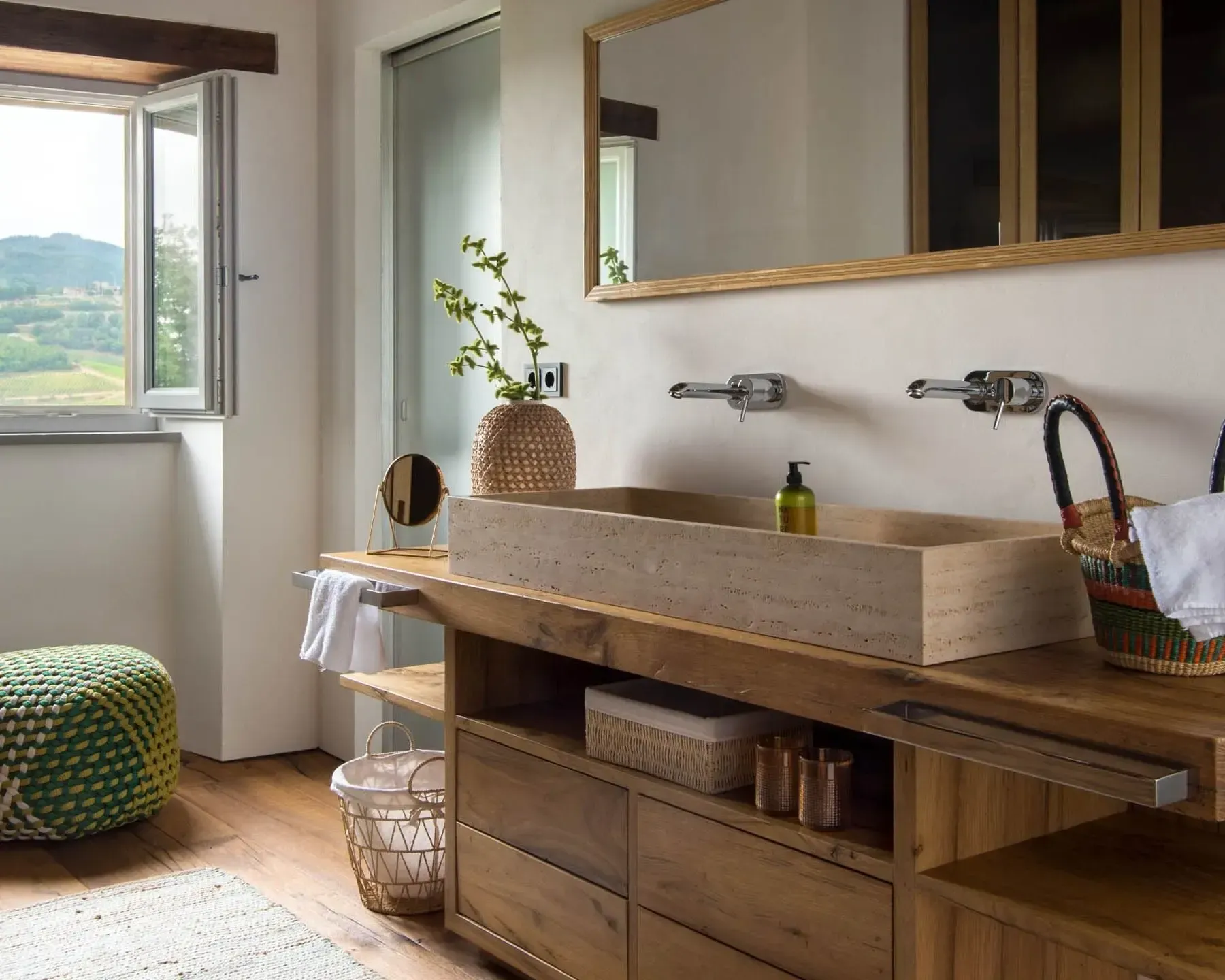 Bathroom with wooden vanity, rectangular sink, mirror, and window with a view.
