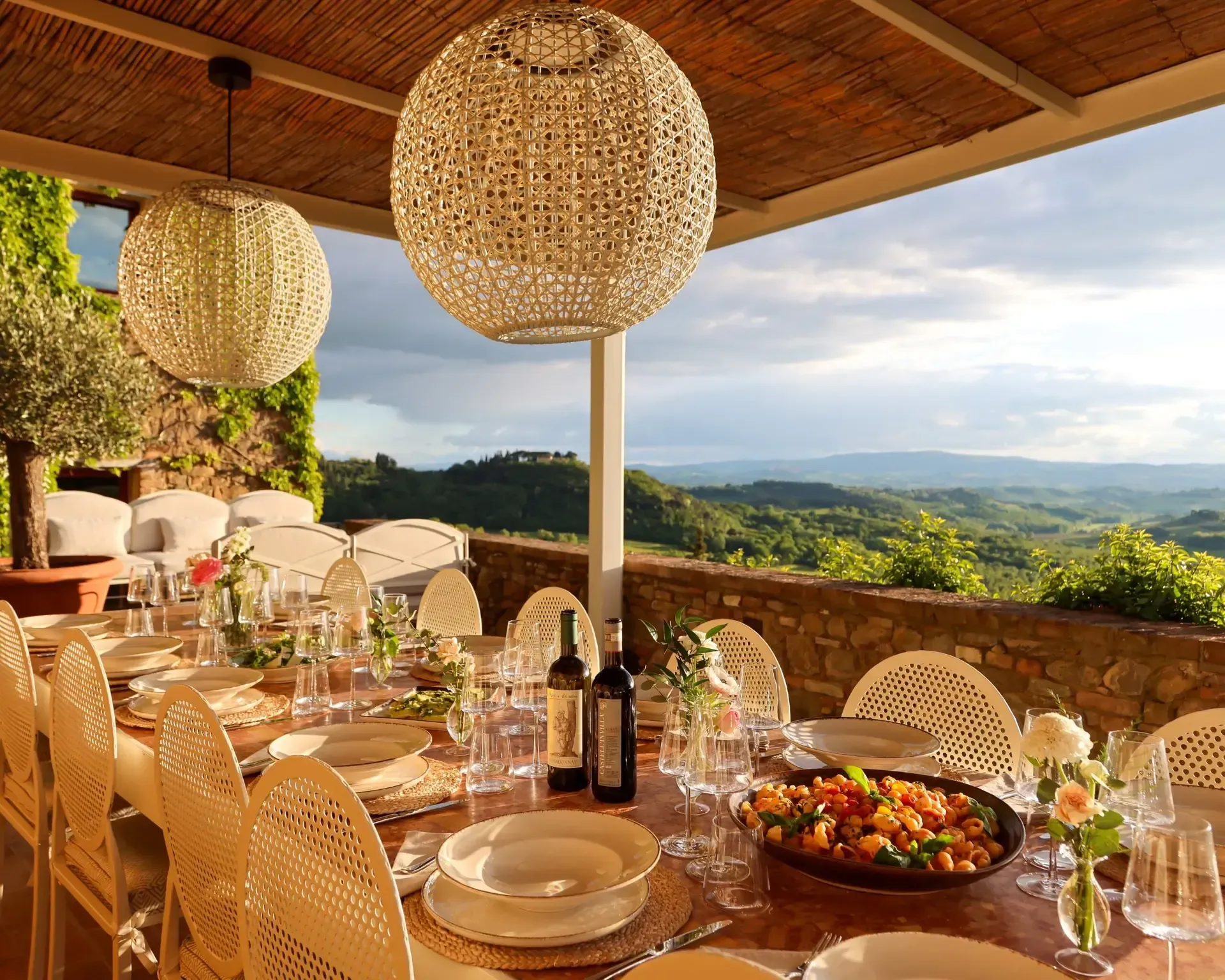 Outdoor dining table set for a meal overlooking a scenic hilltop view, with hanging globe lights.