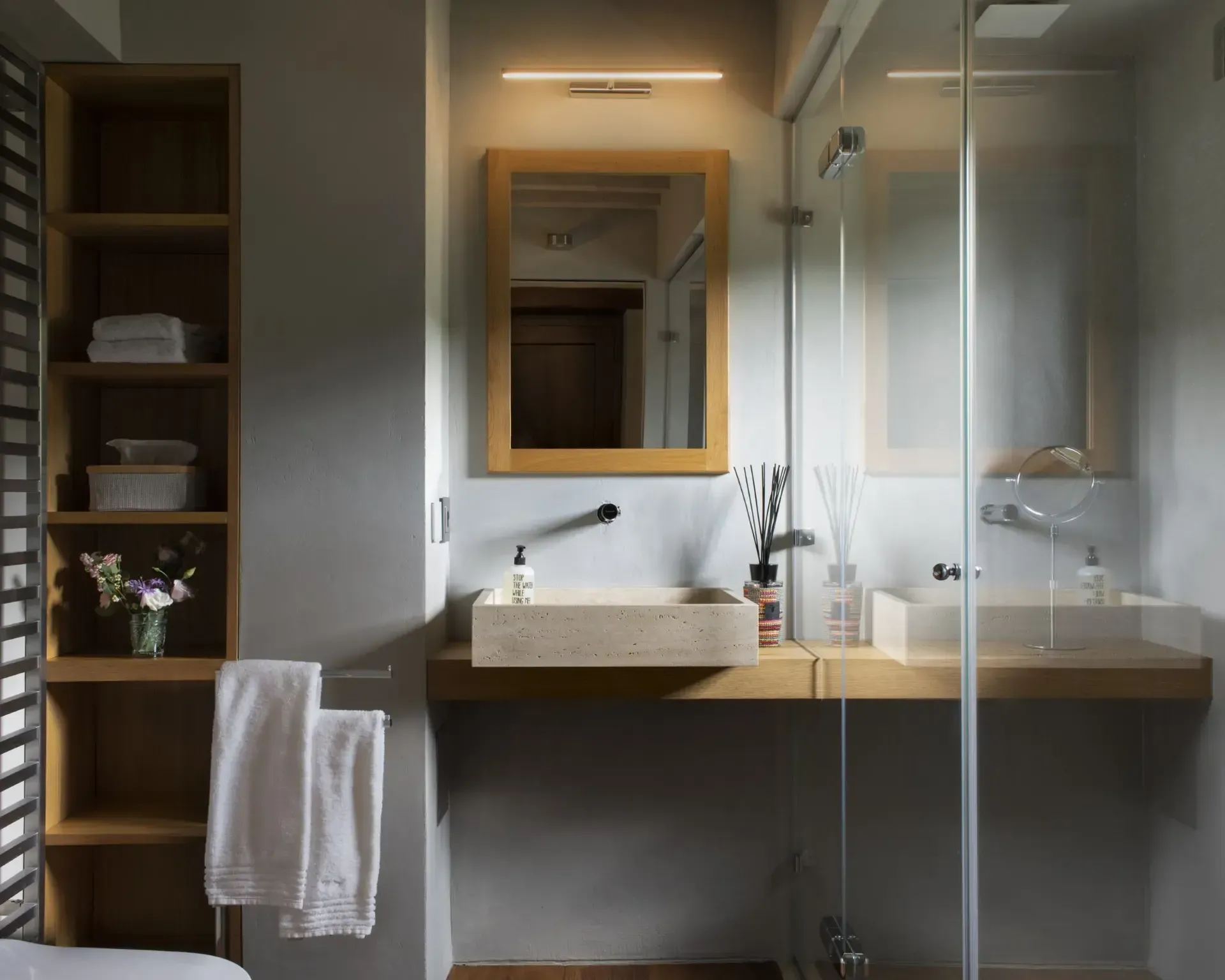 Bathroom with wooden shelves, floating sink, and shower with glass door.