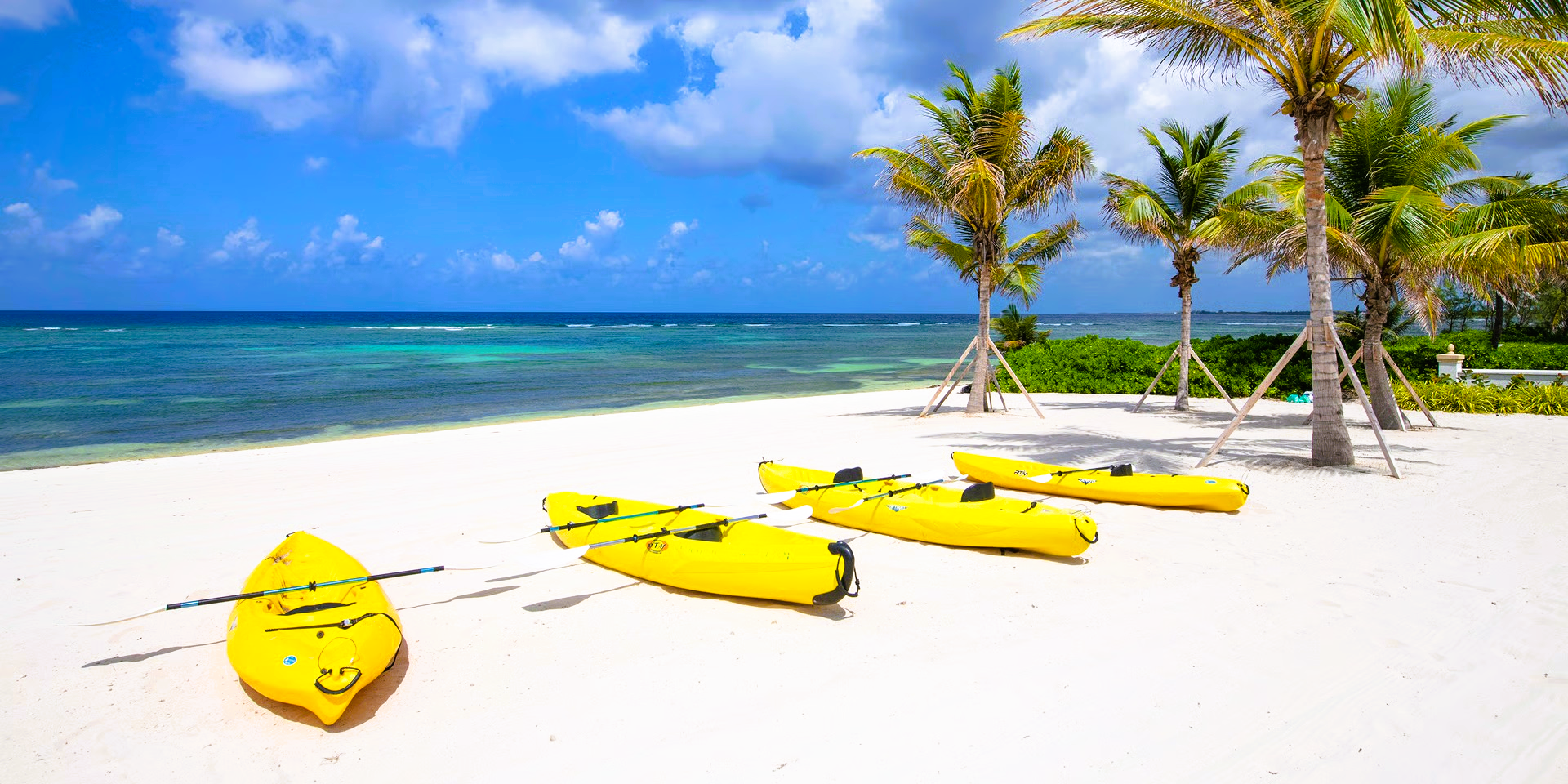 Yellow kayaks on a white sandy beach, with palm trees and a turquoise ocean under a bright blue sky.