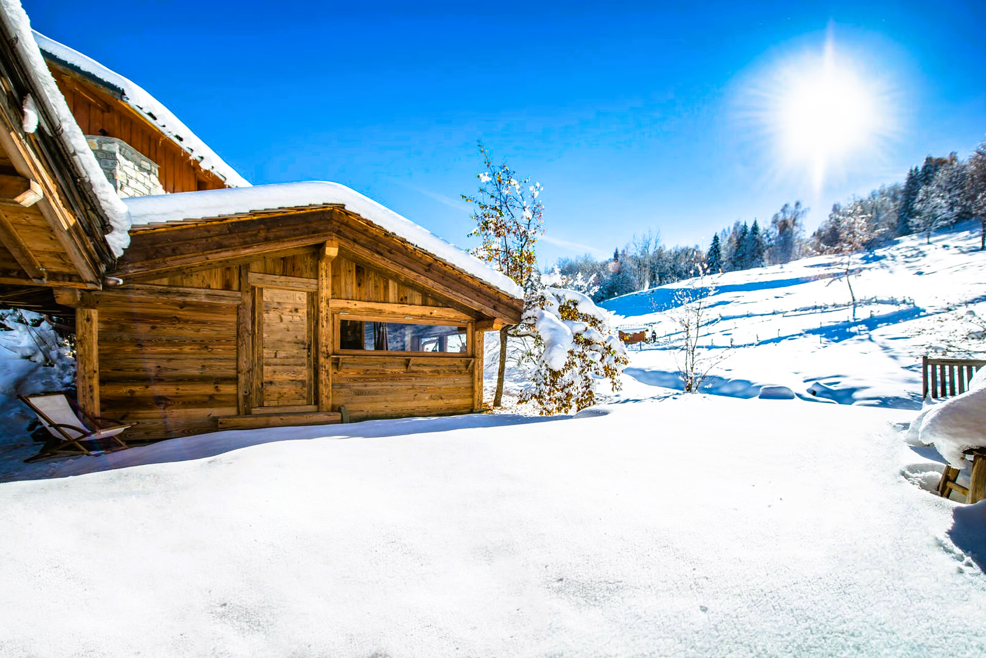 Snow-covered wooden cabin in a sunny, mountainous landscape.