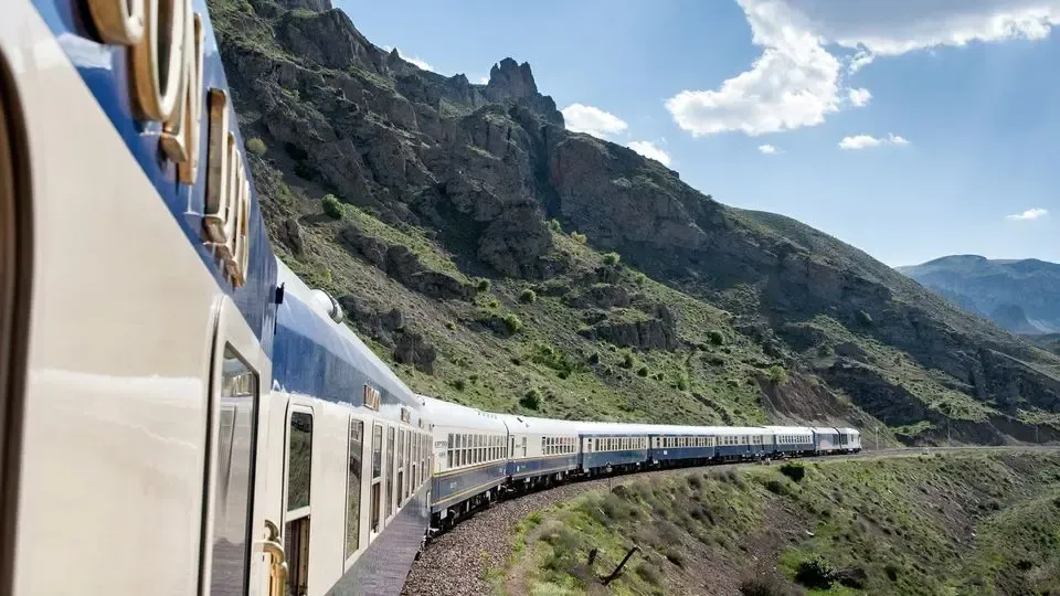 Train traveling along tracks winding through a mountain landscape, blue and white cars.