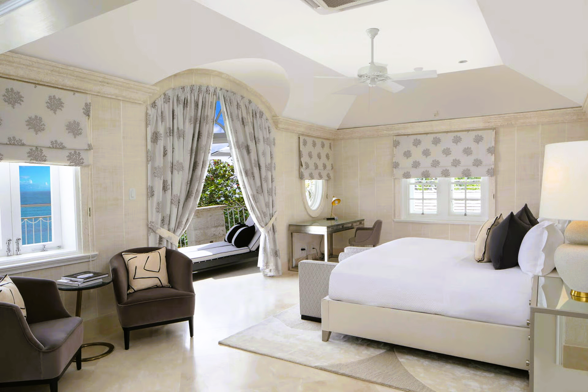 Elegant bedroom with a large bed, seating area, and balcony overlooking the ocean.