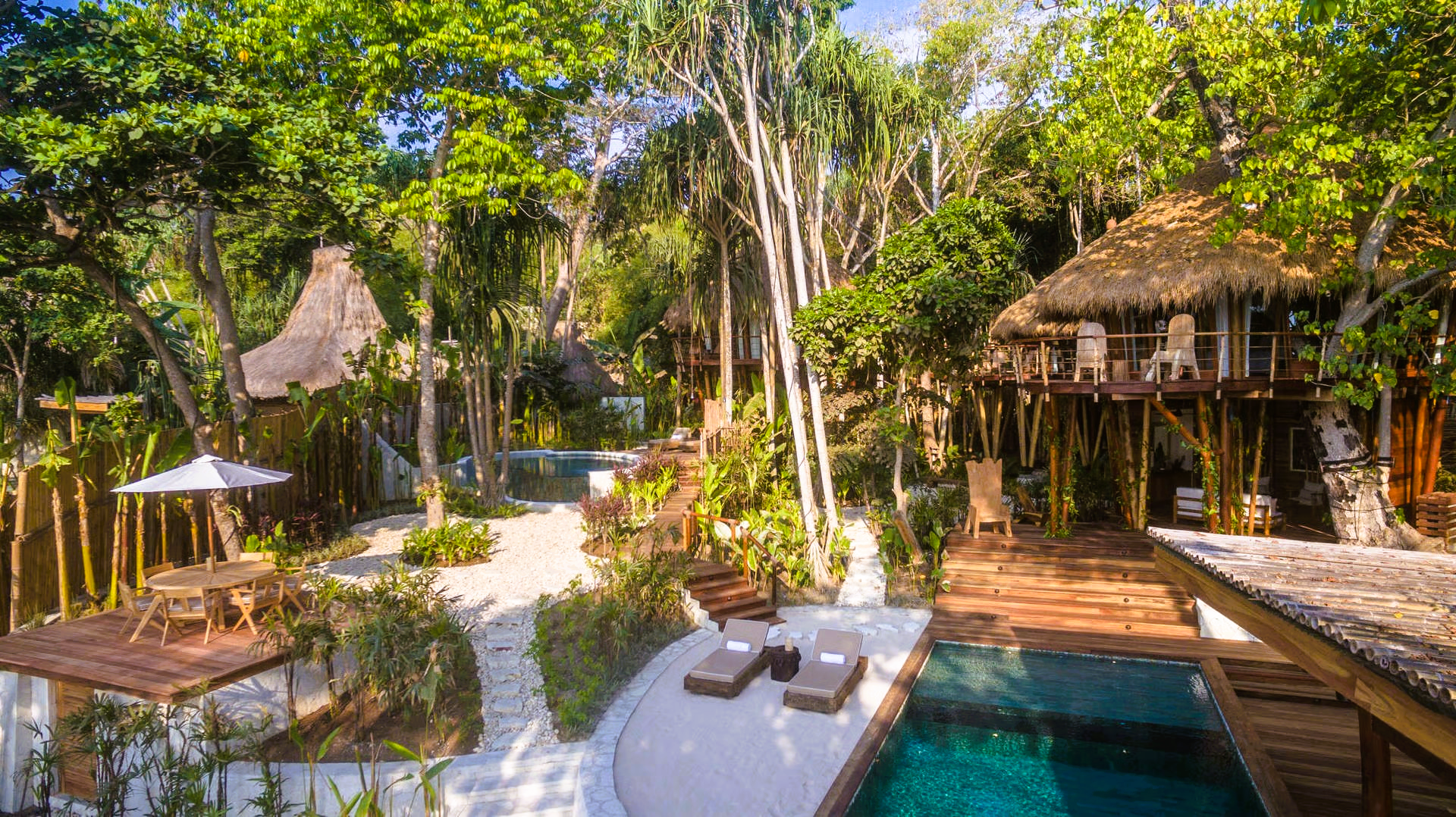Tropical resort with thatched roof huts, pool, and lush greenery.