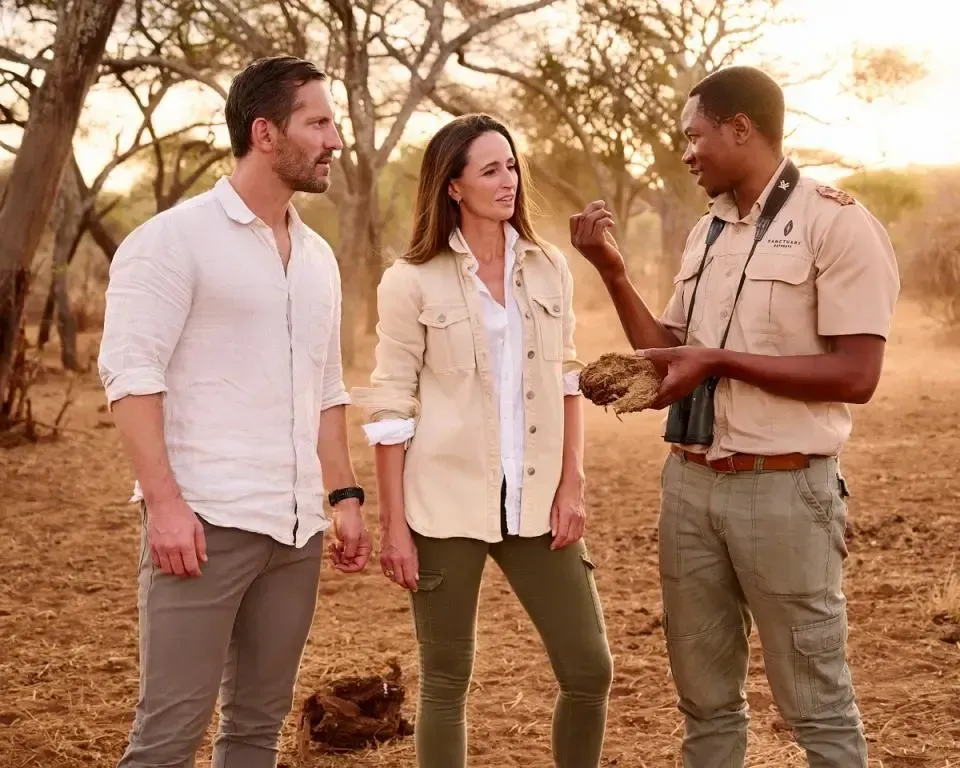 Couple on safari with guide, examining something in the savanna.