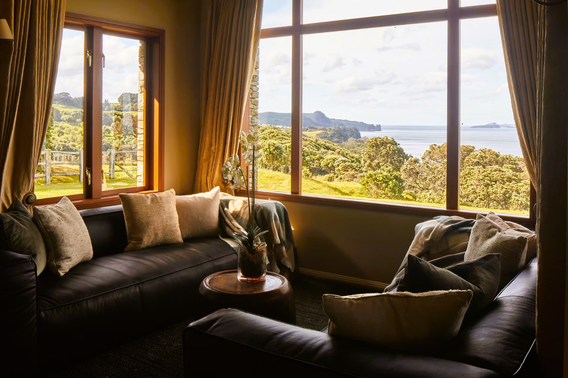 Cozy living room with brown leather couch, large windows overlooking ocean view.