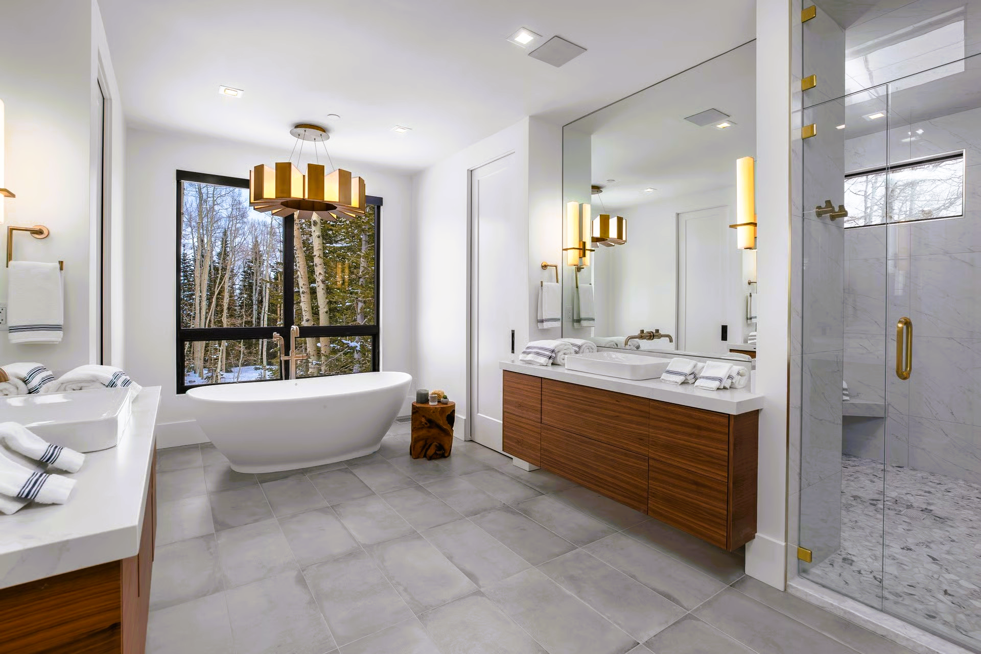 Spacious modern bathroom with a soaking tub, large window with forest view, and marble and wood vanity.