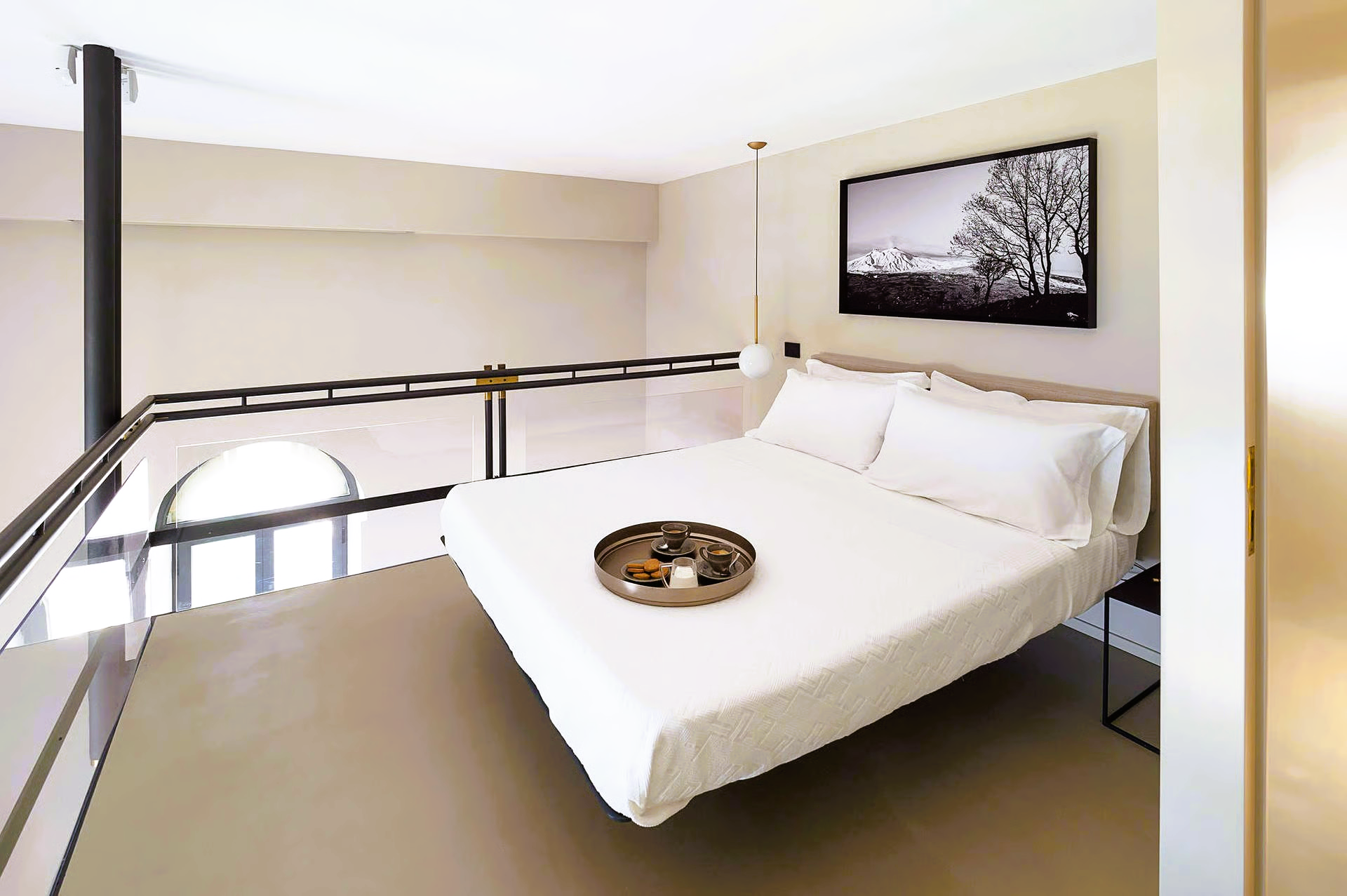 Loft bedroom with white bed, black and white art, balcony, and tray on the bed.