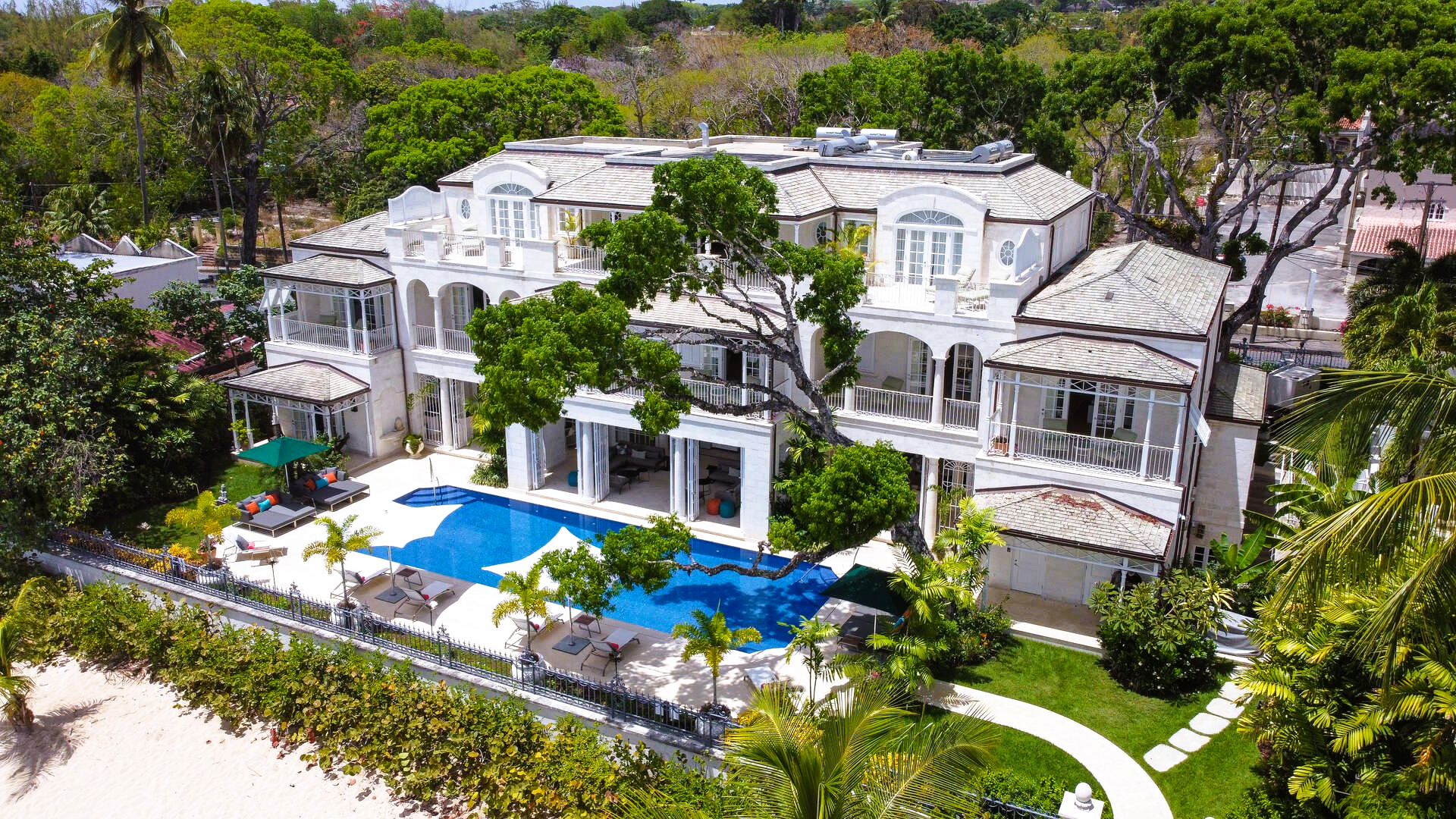 Luxurious white beachfront villa with pool and lush landscaping.