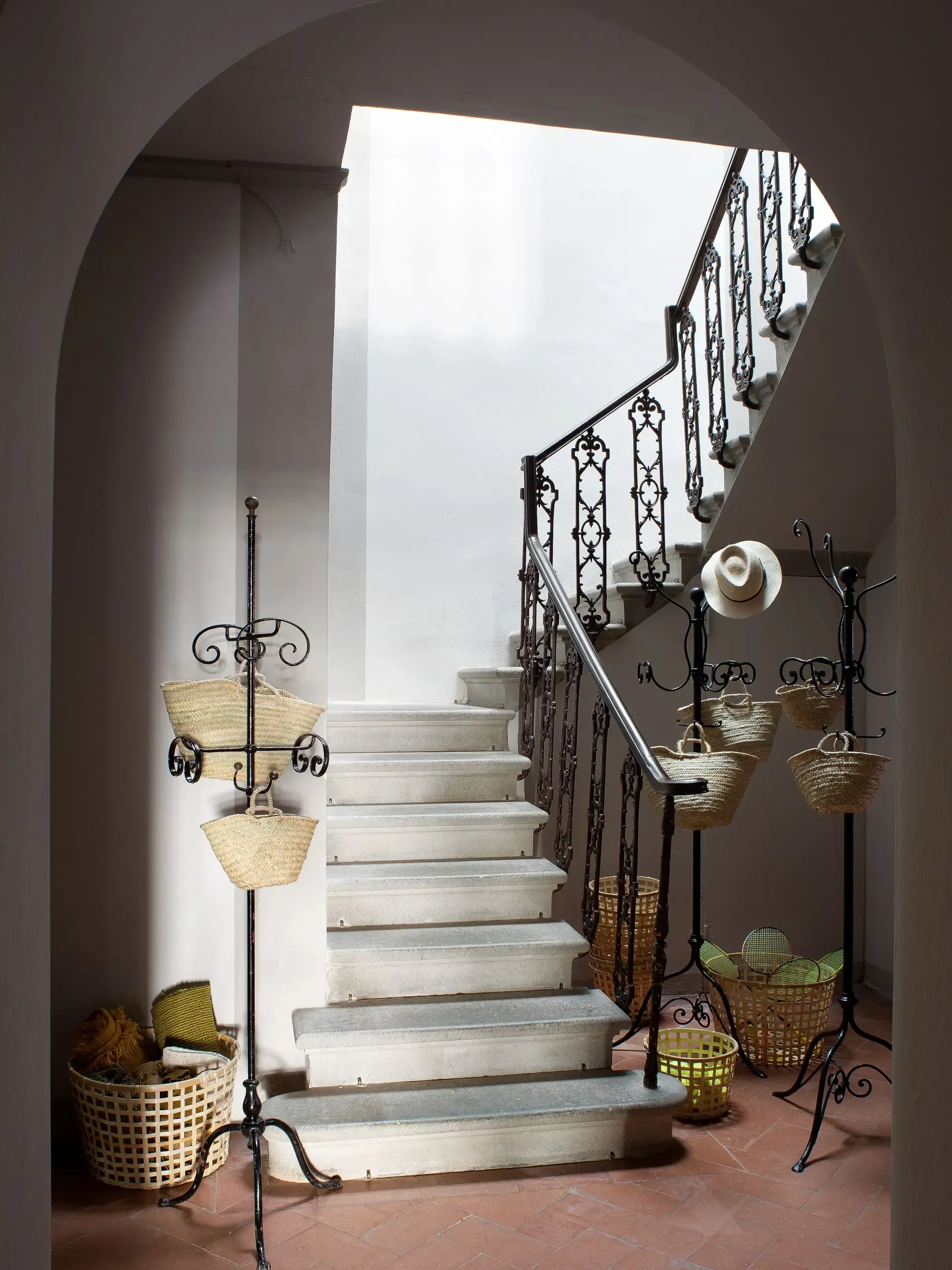 Staircase in a building entrance, white steps, wrought iron railing, baskets on stands, arched doorway.