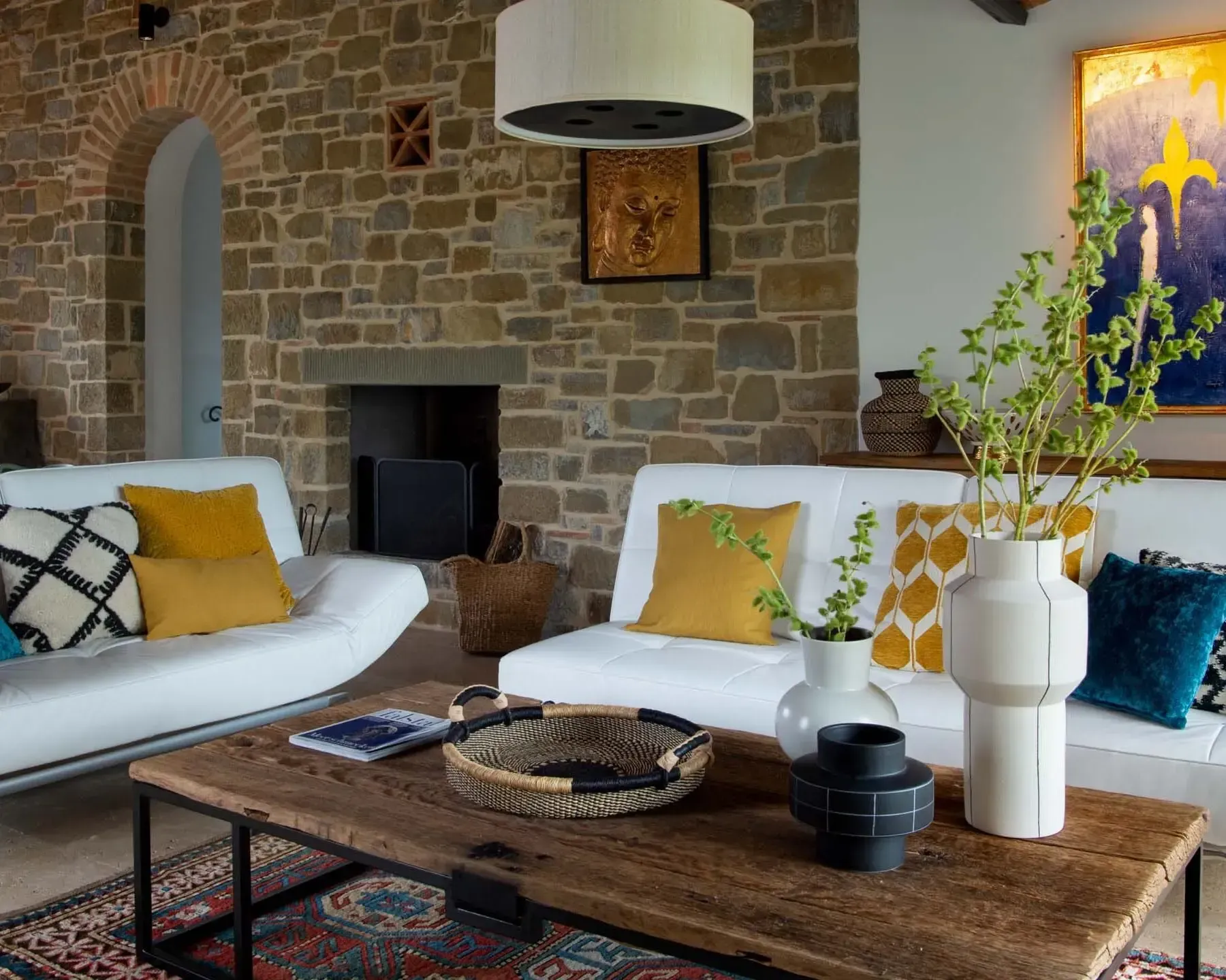 Living room with stone walls, white sofas, wooden coffee table, and colorful pillows.