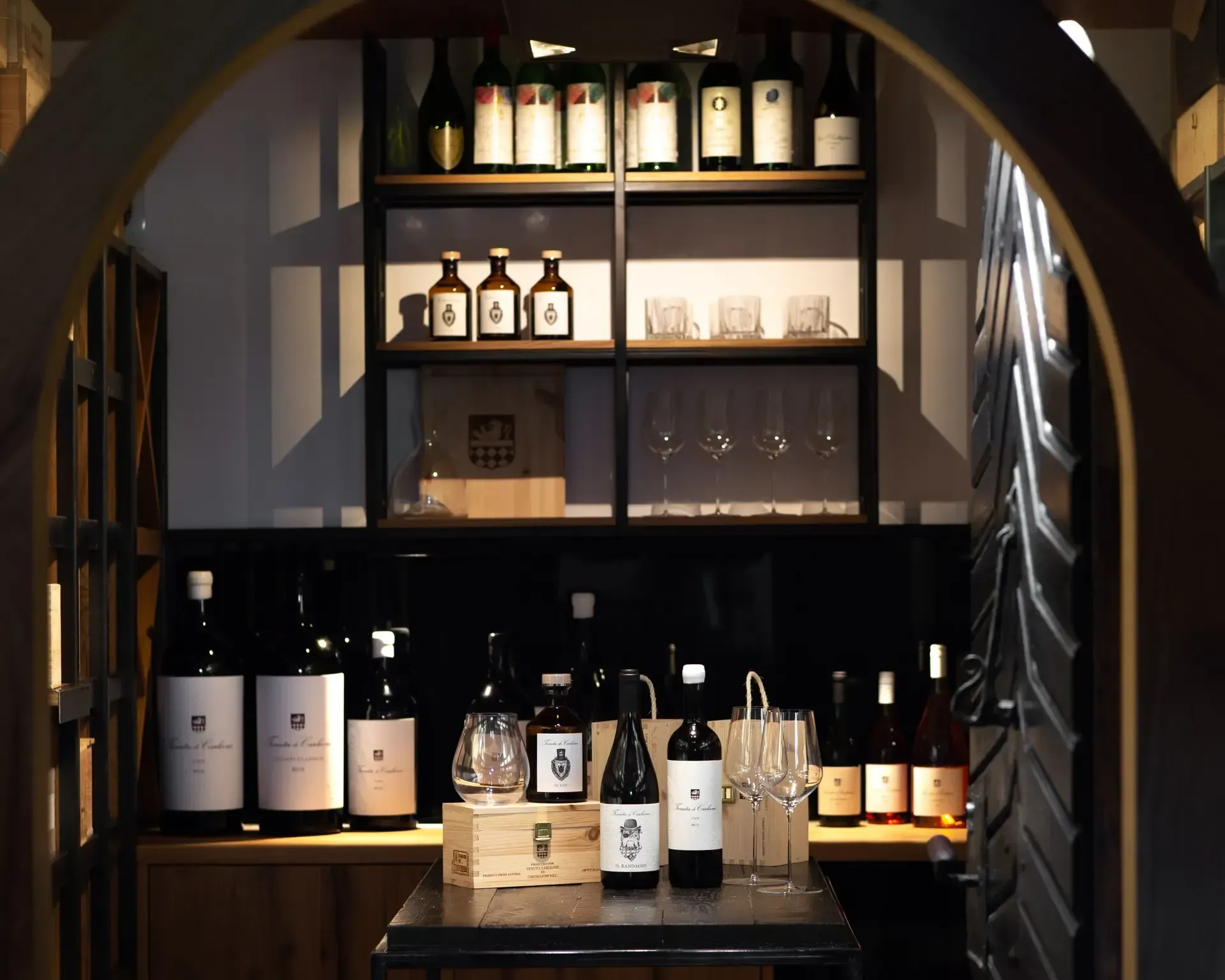 Wine bottles displayed on shelves and a table inside a dimly lit archway.