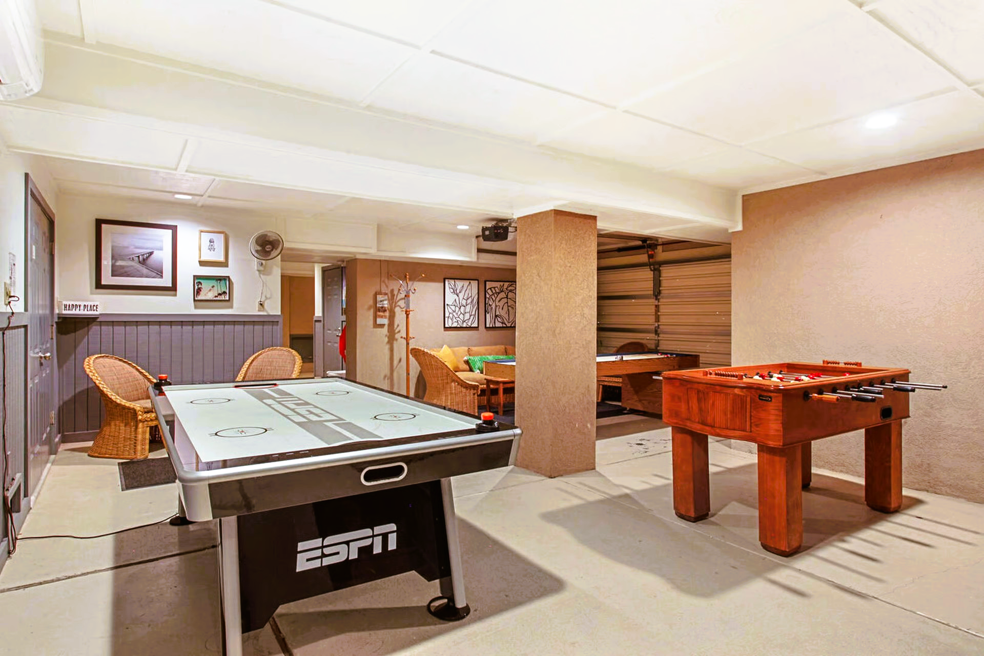 A game room with an air hockey table and foosball table. Brown and neutral tones, recessed lighting.