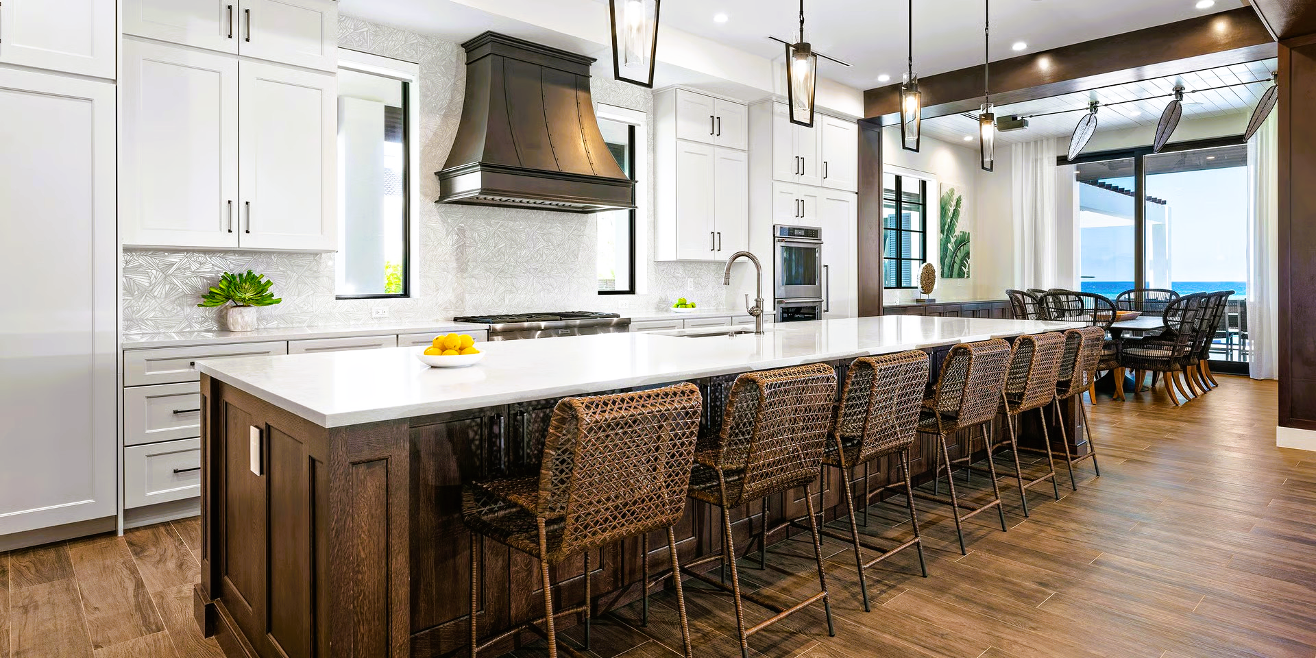 A modern kitchen with a large island, dark wood cabinets, white countertops, and wicker bar stools.