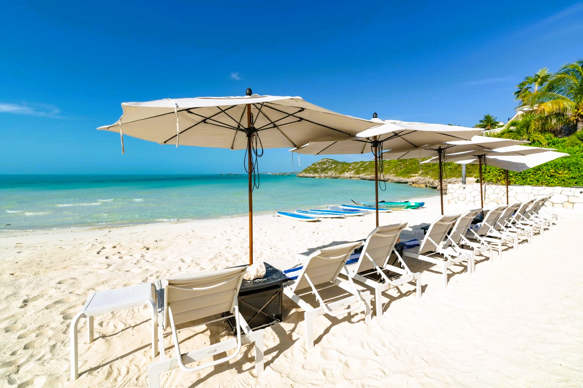 Beach scene with lounge chairs and umbrellas along the white sand, ocean in the background, sunny day.