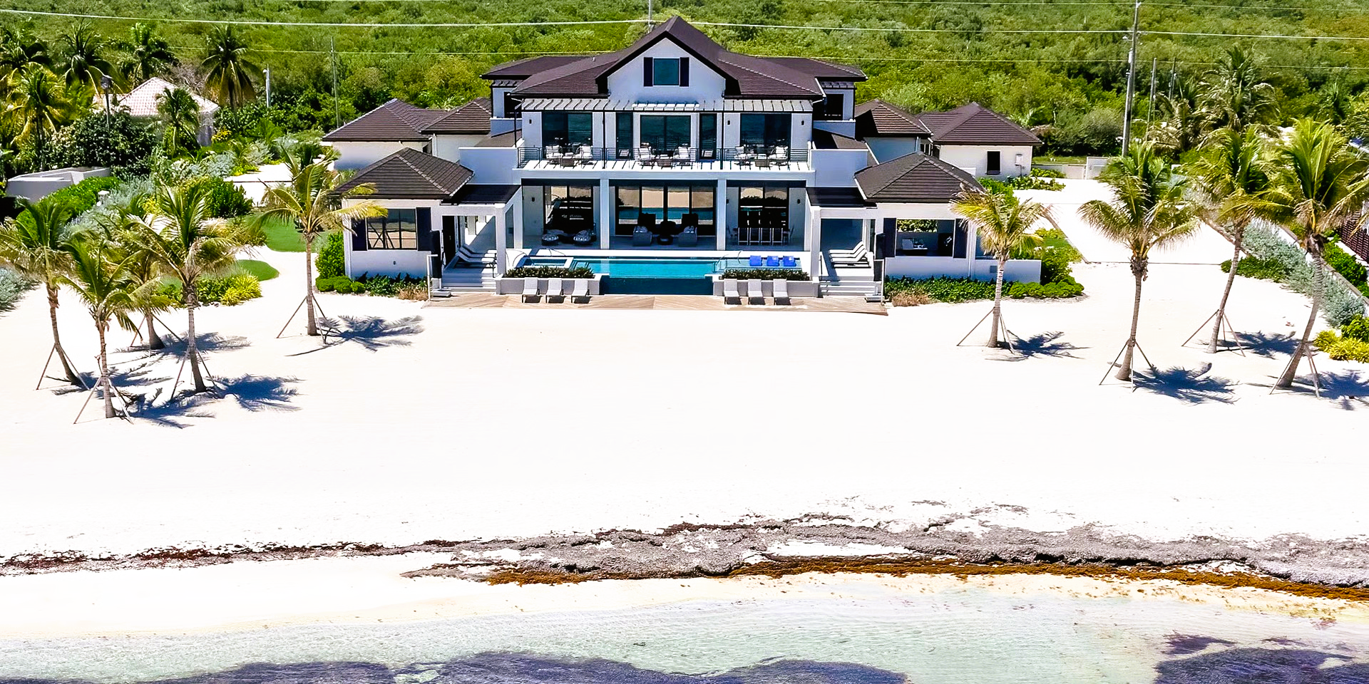 Beachfront mansion with white facade and palm trees on white sand.