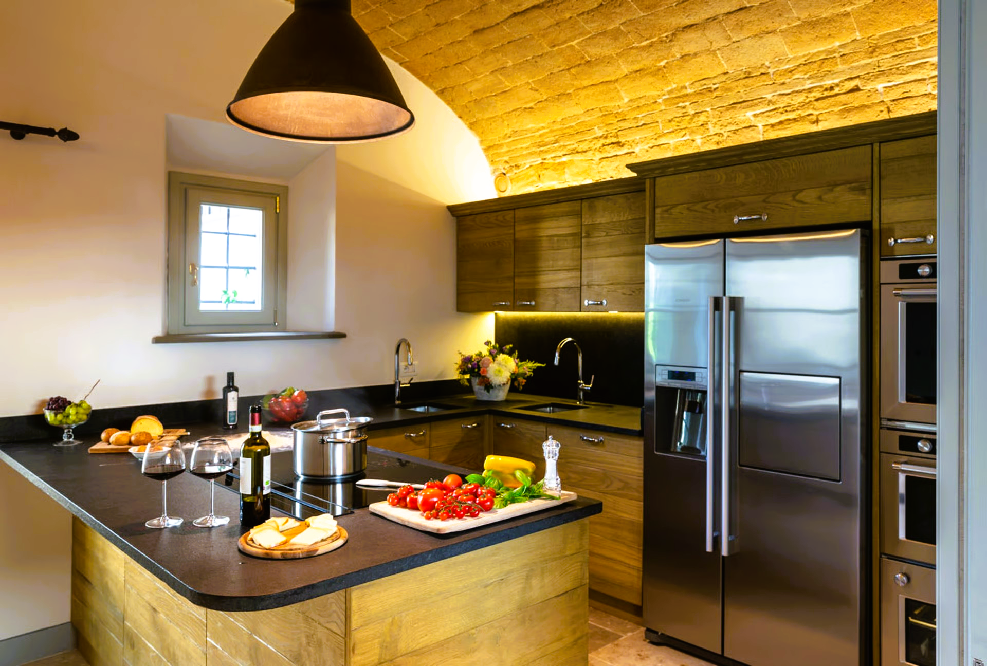 Kitchen with stainless steel appliances, dark countertops, and a wooden island with food.