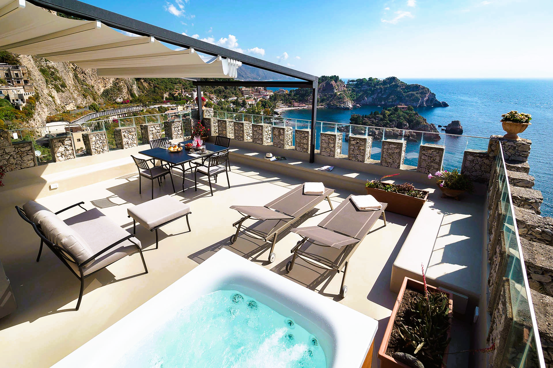 Terrace with ocean view, featuring a jacuzzi, lounge chairs, table, and pergola. Blue sky and water.