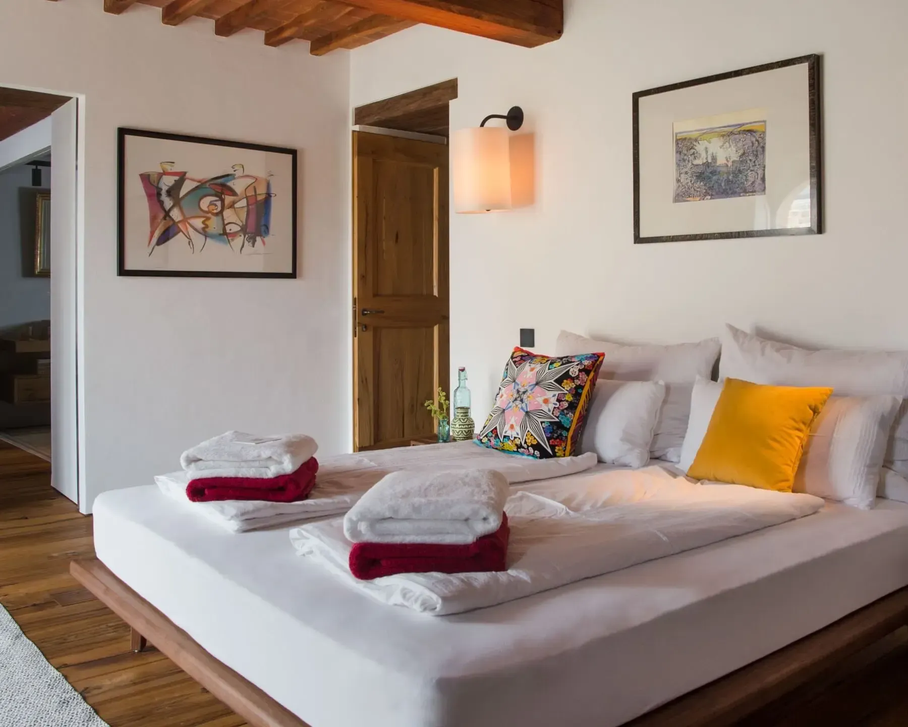 Bedroom with a large bed, artwork on the walls, and a wooden ceiling.