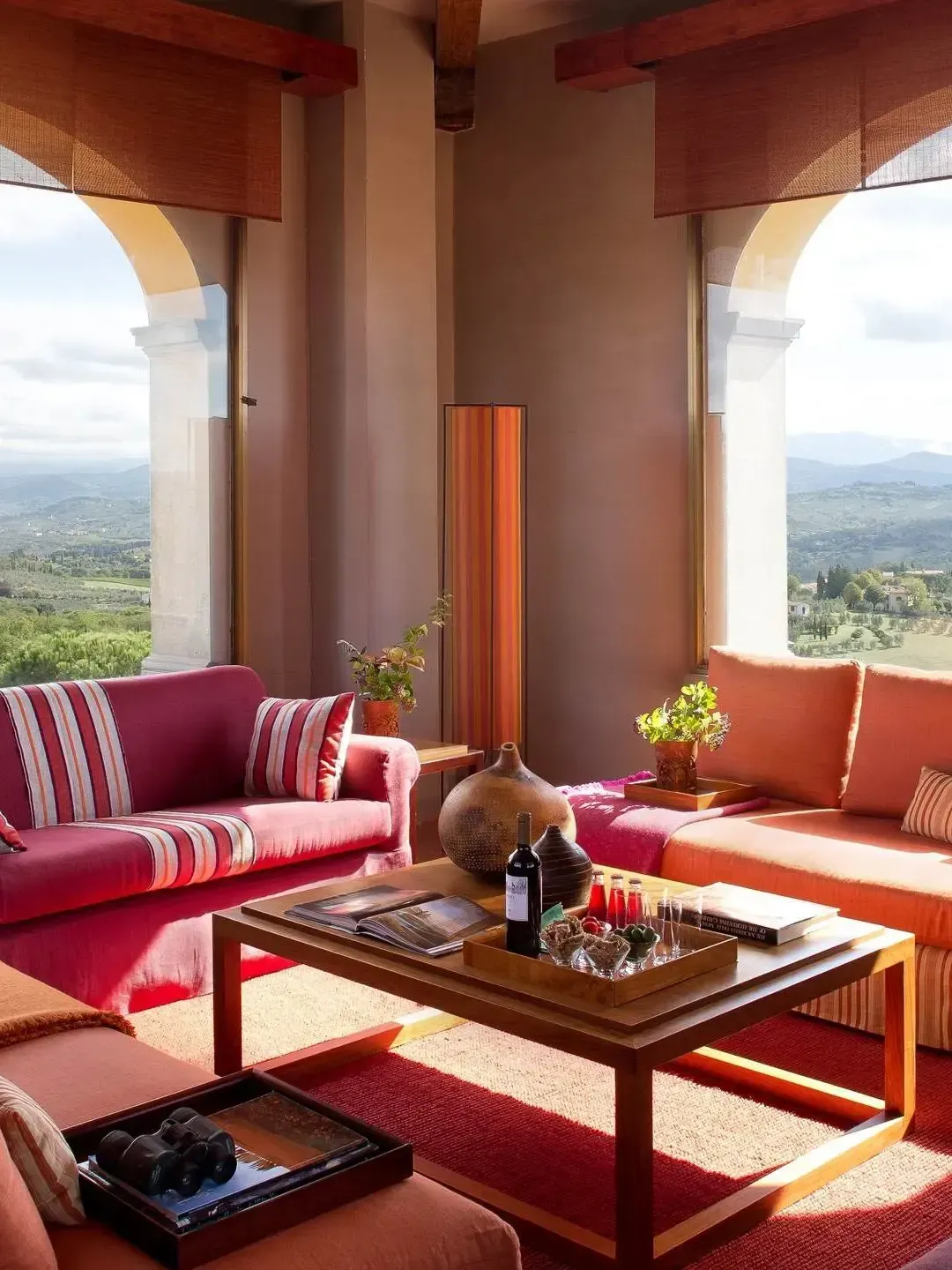 Living room with red couches, coffee table, and arch windows overlooking a green landscape.